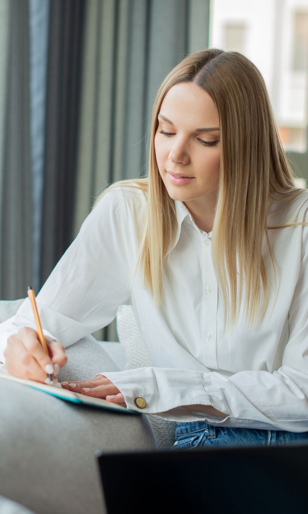 mujer escribiendo en un cuaderno en su casa, junto a una ventana