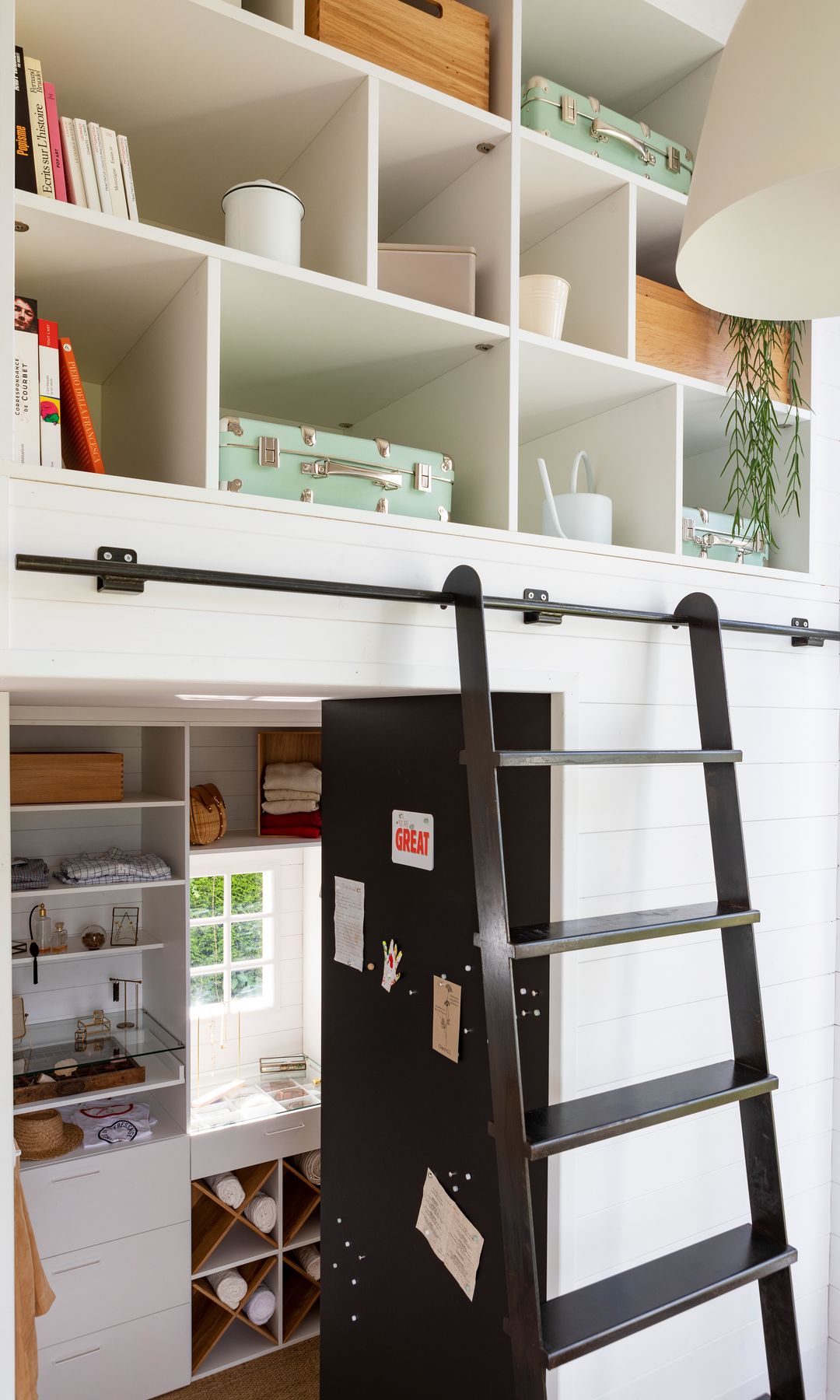 Entrada con hueco de almacenaje abierto con maletas, cestos y libros, escalera metálica negra 