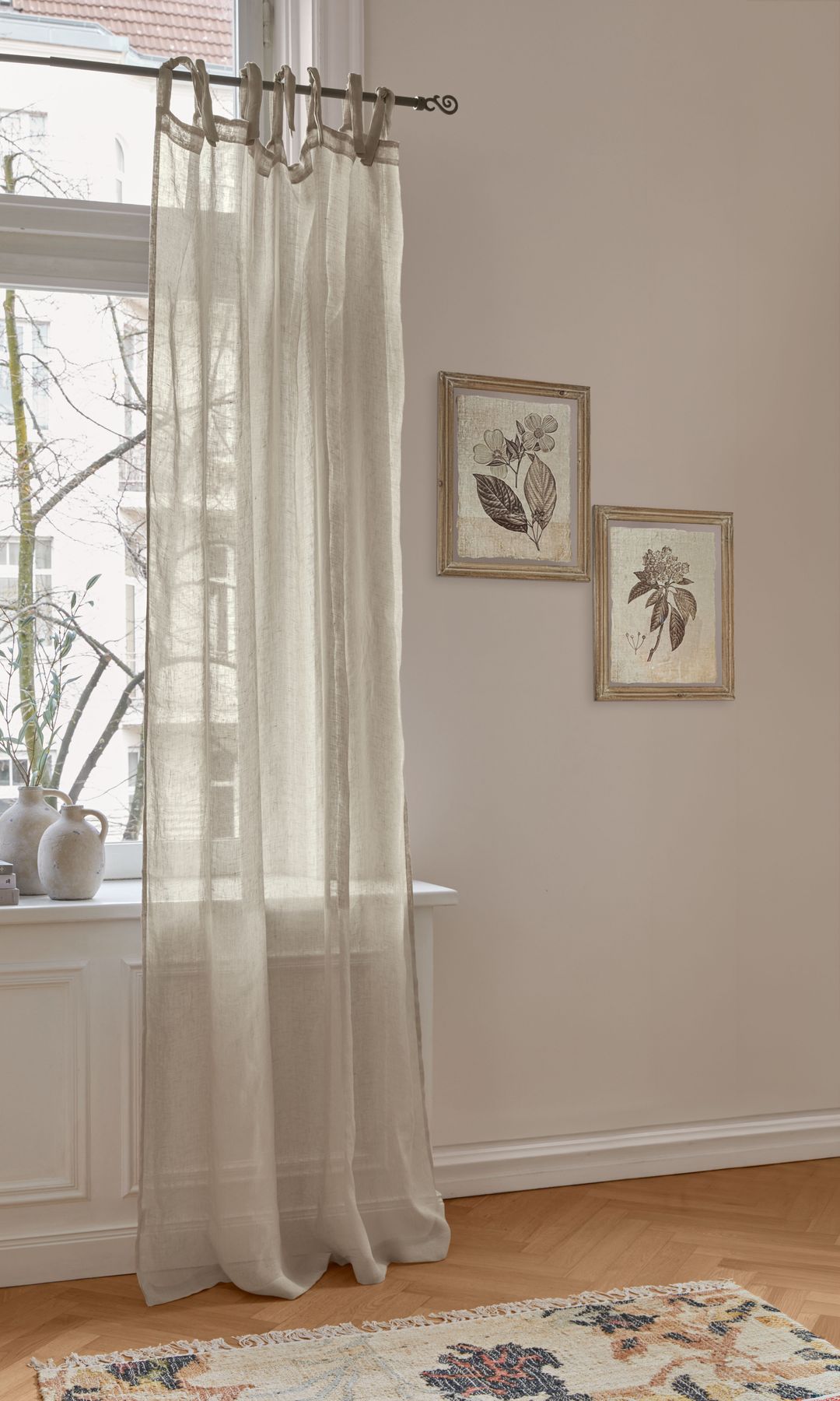 Rincón junto a la ventana con paredes en color beige, cuadros en la pared, cortinas del mismo color transparentes, alféizar ventana