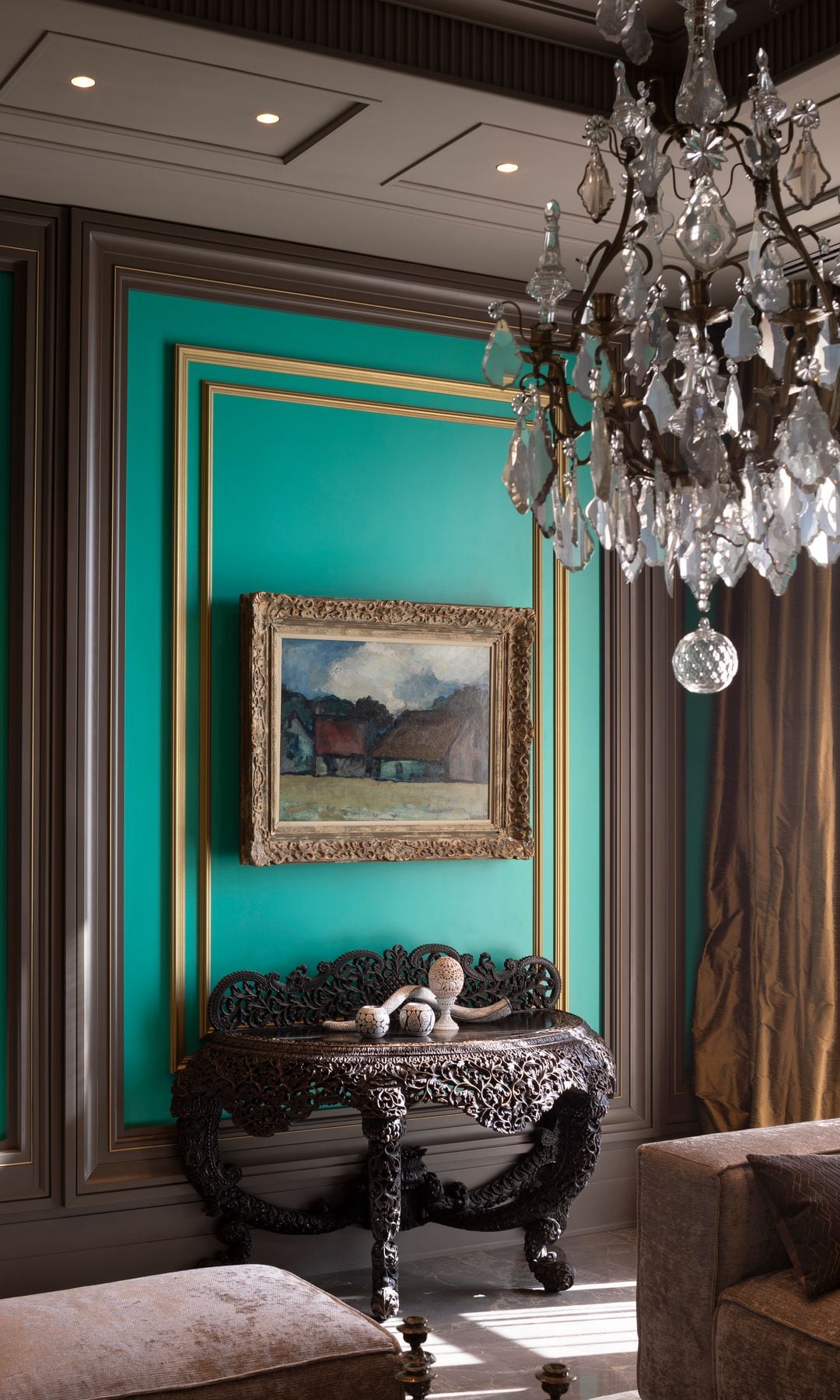 Salón con paredes verdes con molduras, lámpara de techo de cristal, consola con las patas torneadas, cuadro en la pared, puf