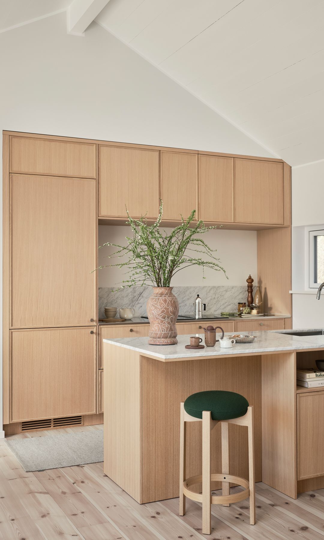 Cocina abierta de madera con isla con zona de barra, frigorífico integrado, jarrón con ramas verdes