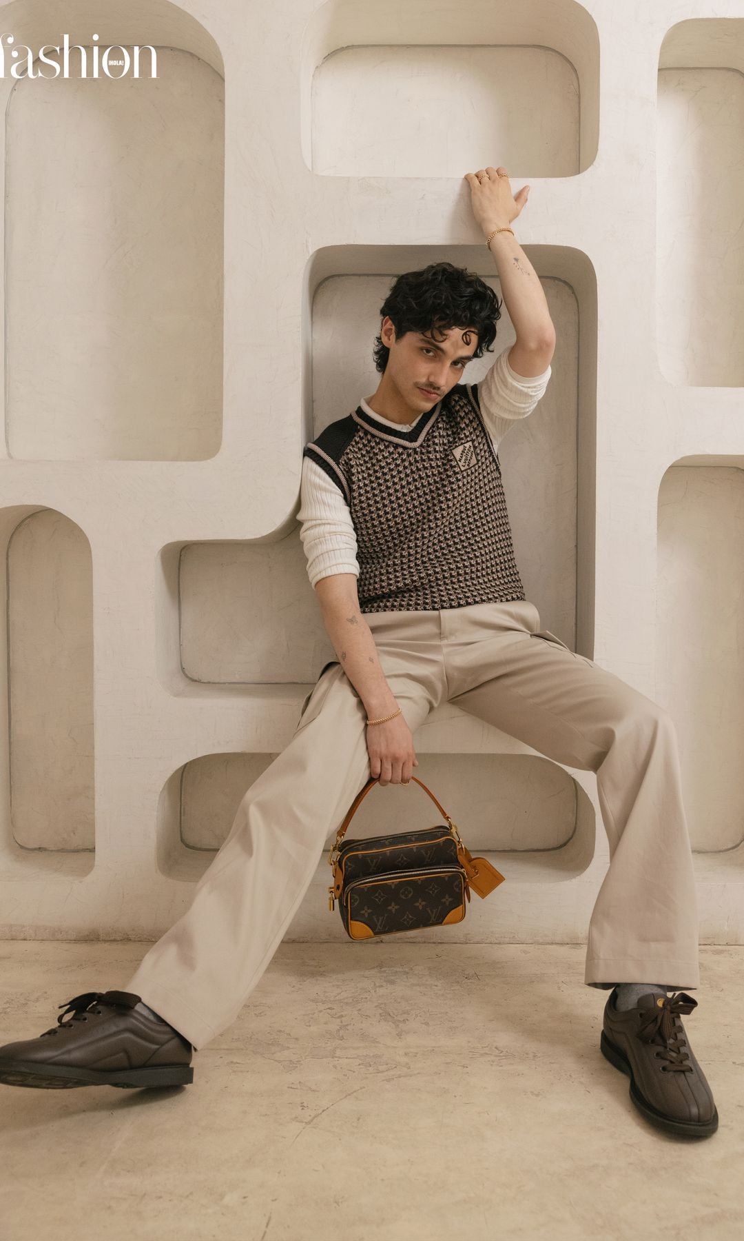 HUMBE, reconocido por su impacto y trayectoria, aparece con un total look de Louis Vuitton, compuesto por chaleco de punto y pantalones de vestir, complementado con brazaletes y anillos de la colección «Clash» de Cartier.