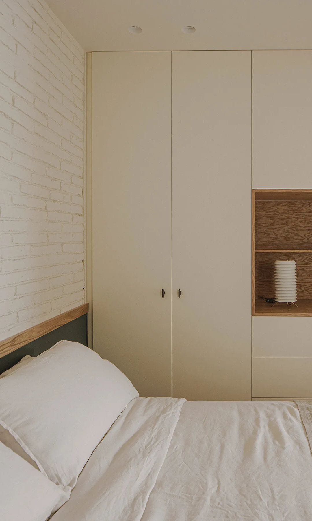 Dormitorio con pared del cabecero de ladrillo blanco, armario hasta el techo blanco, con hornacina de madera, cabecero con zócalo alto