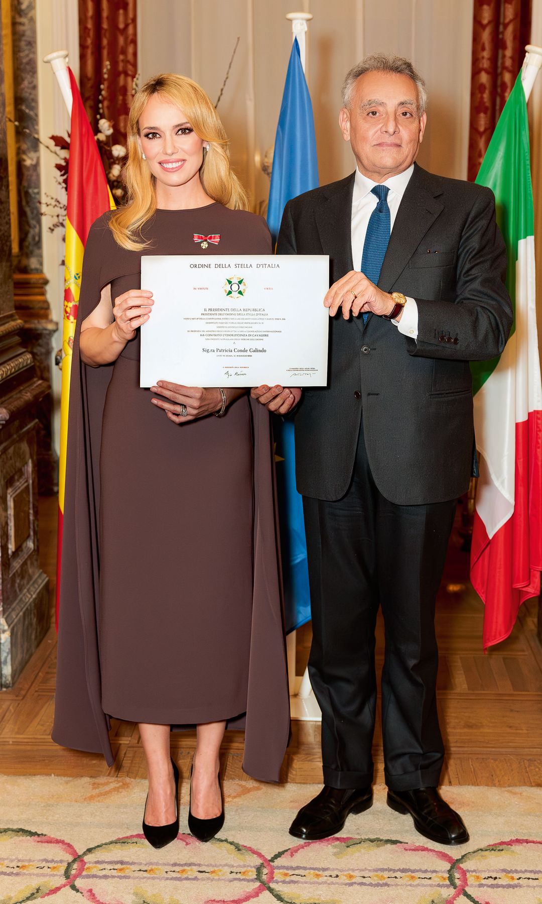 Patricia Conde recibiendo las insignias, entregadas por el embajador Giuseppe Buccino Grimaldi, con quien posa con el diploma que acredita el nombramiento 