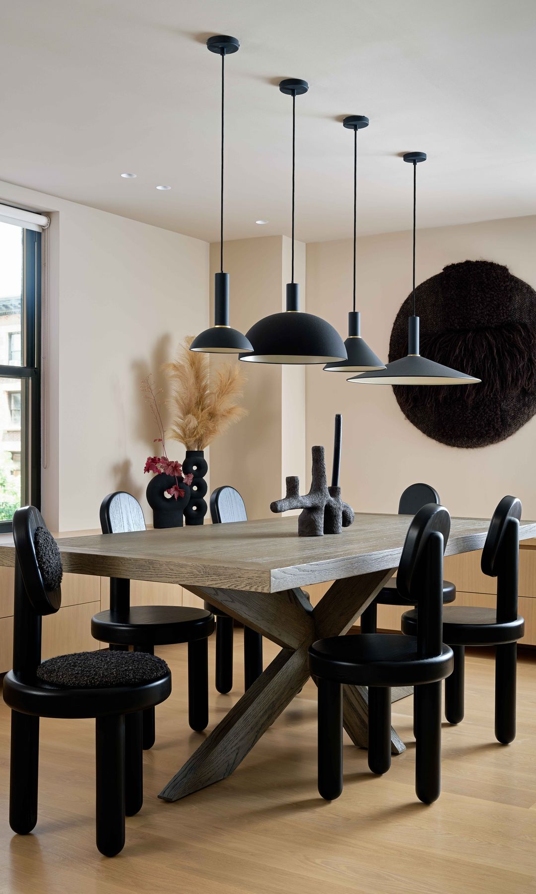 Comedor con mesa con las patas negras, sillas negras de tres patas, lámparas de techo negras, suelo de madera, aparador 