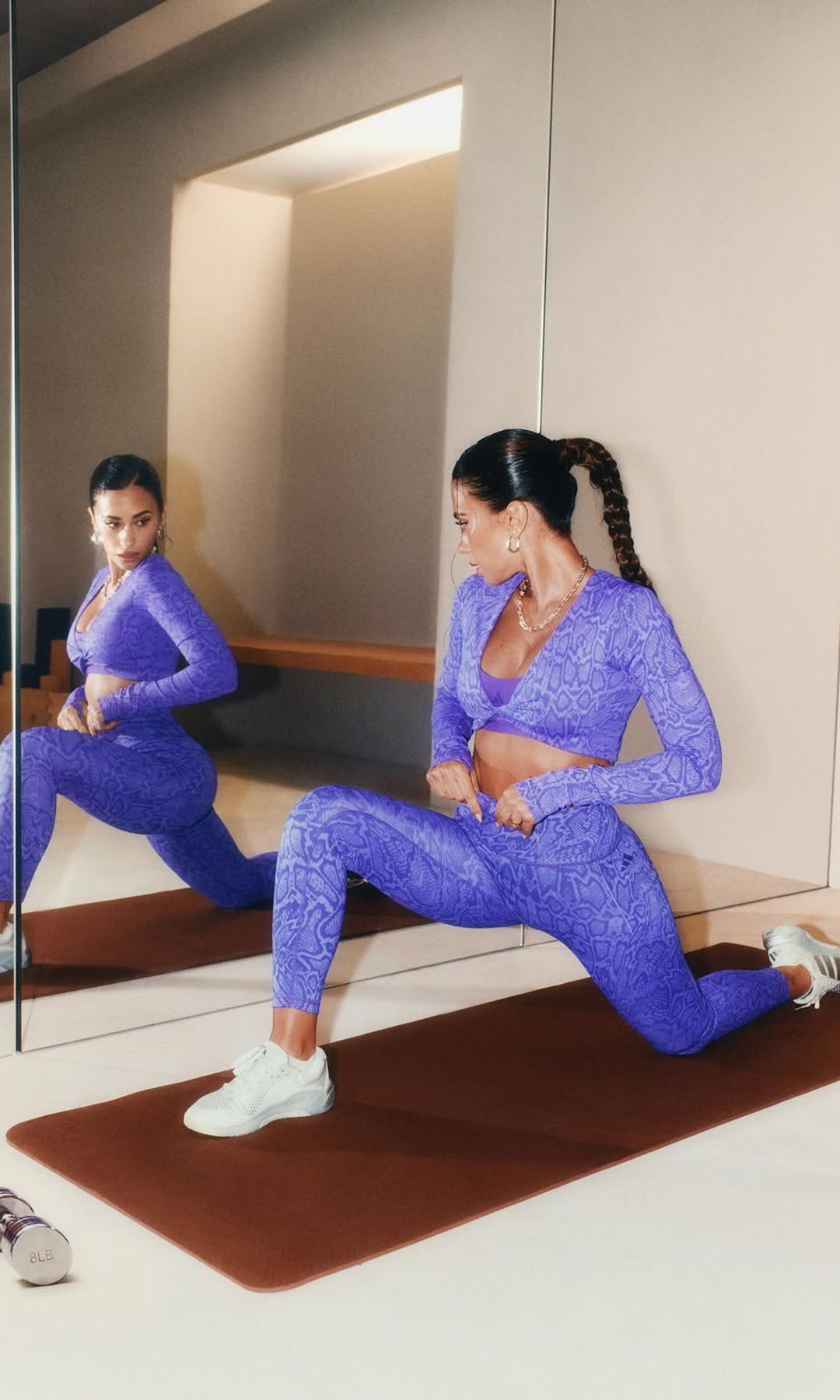 Antonela Roccuzzo estira sobre una esterilla frente a un espejo con ropa deportiva morada.
