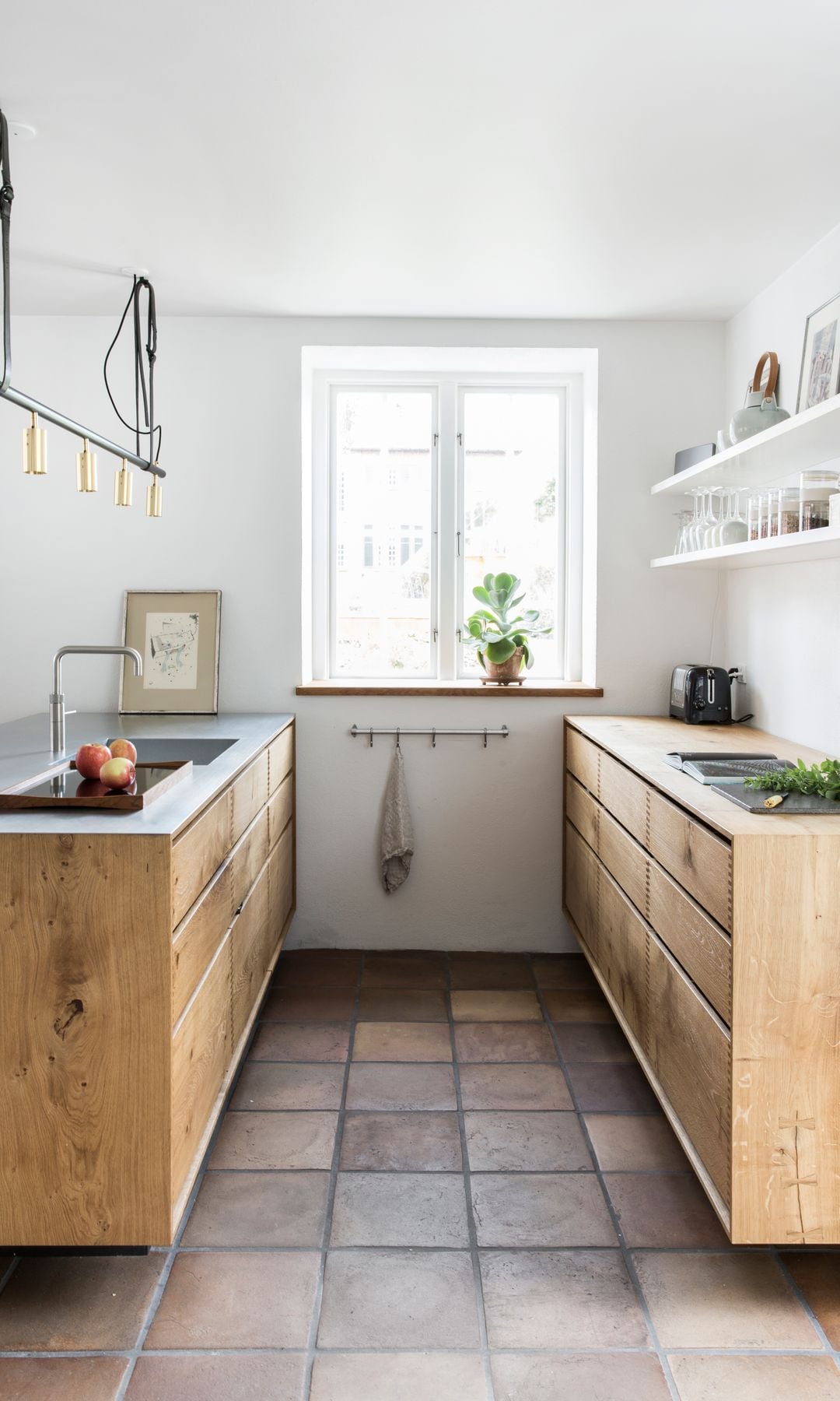 Cocina de madera en paralelo con suelos de barro, sin armarios altos, baldas blancas, ganchos para los trapos de cocina, lámpara de techo