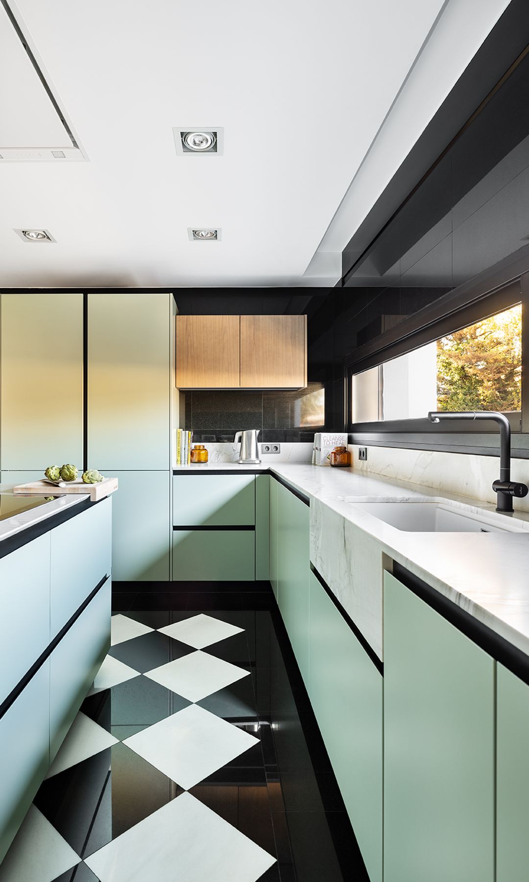 Cocina con los muebles verdes claro, el suelo de damero blanco y negro, encimera blanca y electrodomésticos integrados