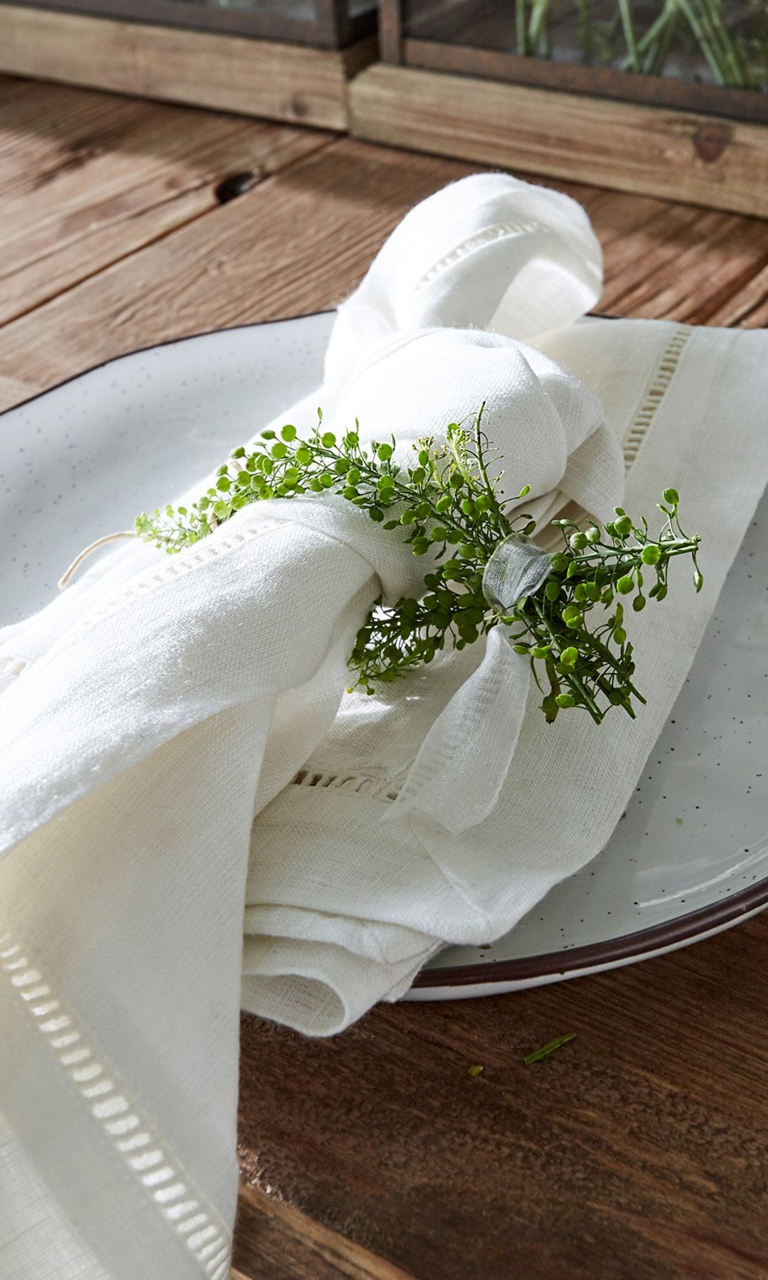 Mesa de madera con plato de cerámica, servilletas blancas de lino anudadas con una cinta y un ramillete