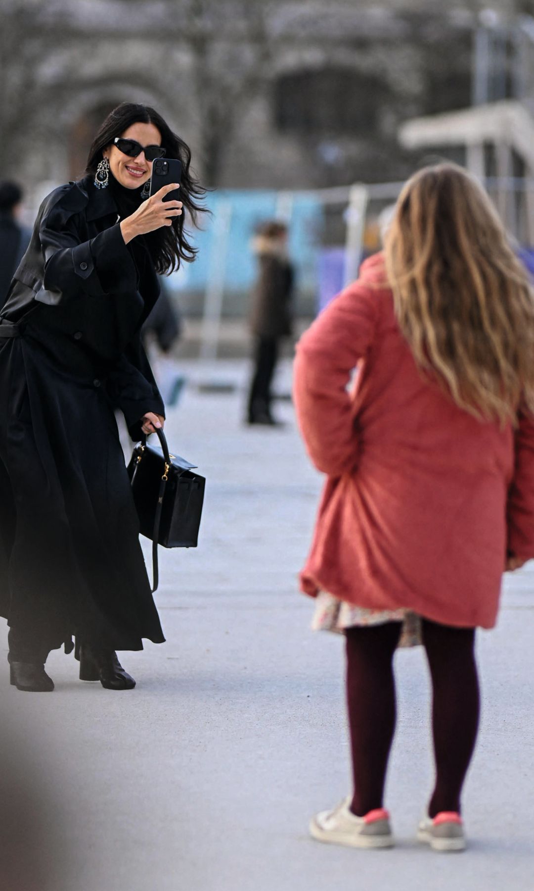 Irina Shayk, con abrigo negro y gafas de sol, toma una foto con su teléfono.