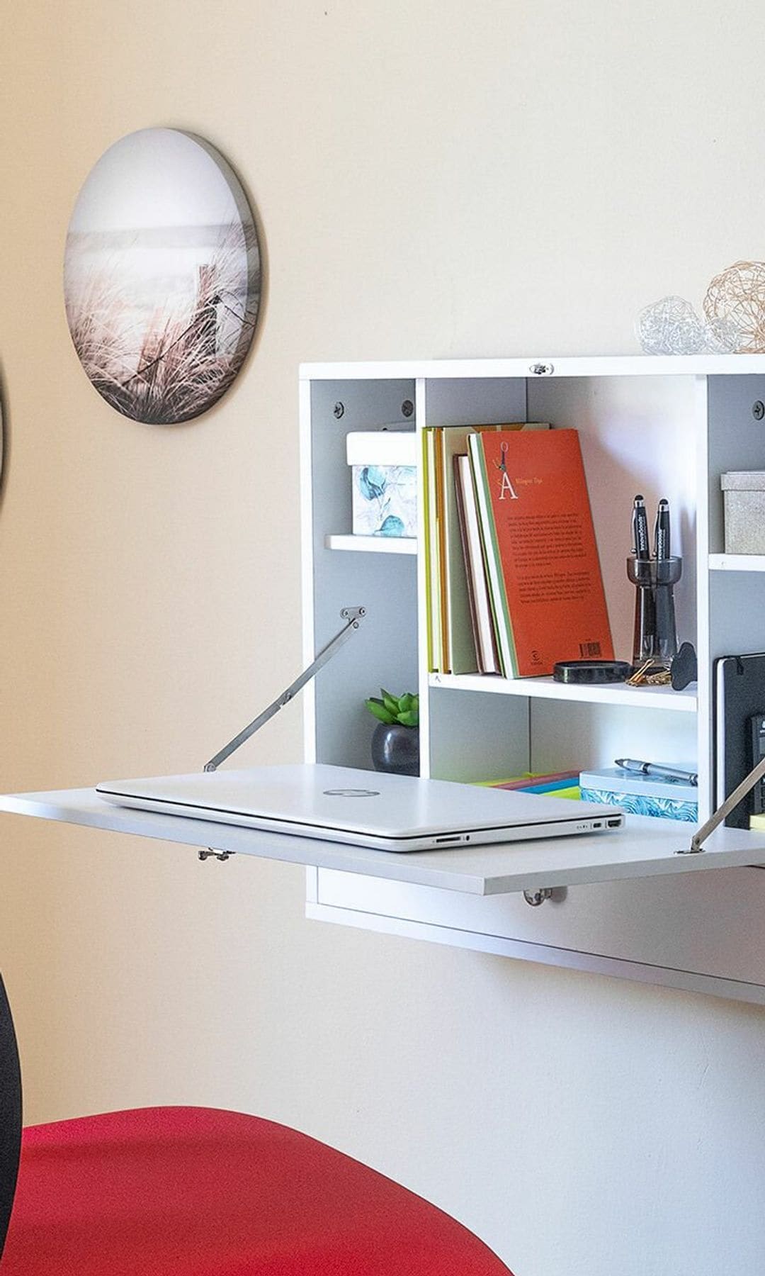 Escritorio plegable de pared de color blanco, con silla tapizada roja y cuadros