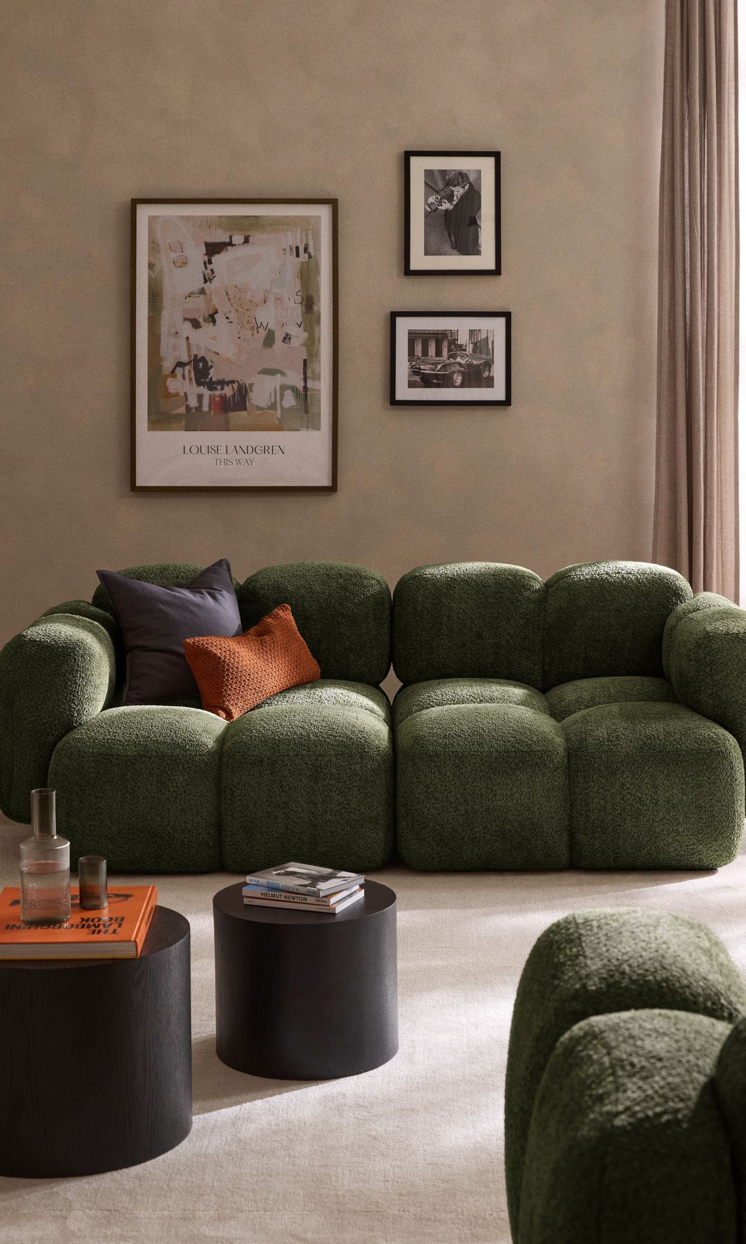 Salón con sofá verde de formas orgánicas, mesas auxiliares negras, cuadros en la pared, cojines sobre el sofá