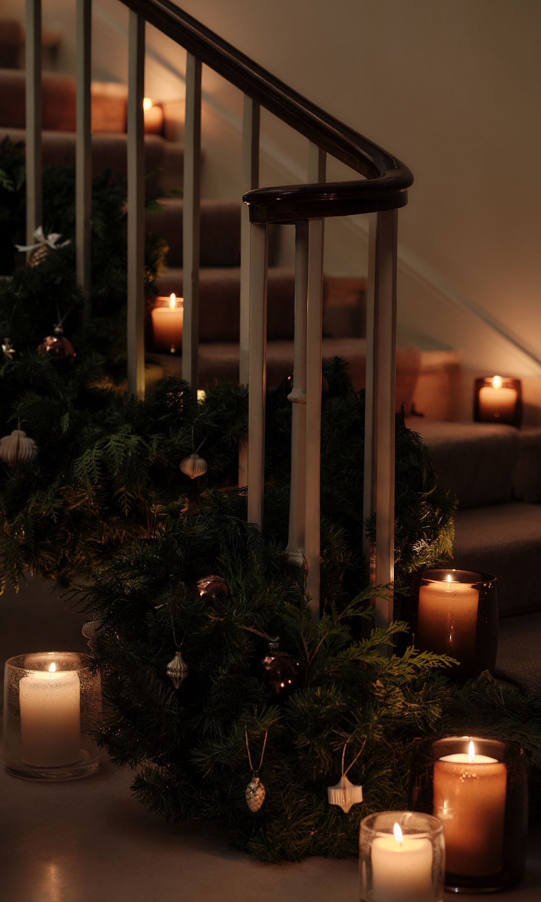 Escalera de una casa con decoración navideña, guirnaldas en la barandilla y velas en los escalones