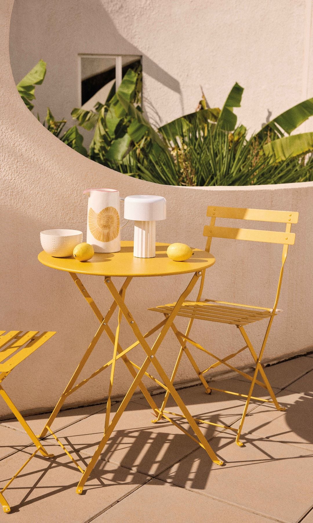 Mesa y sillas de jardín metálicas en color amarillo, lámpara portátil blanca y jarrón