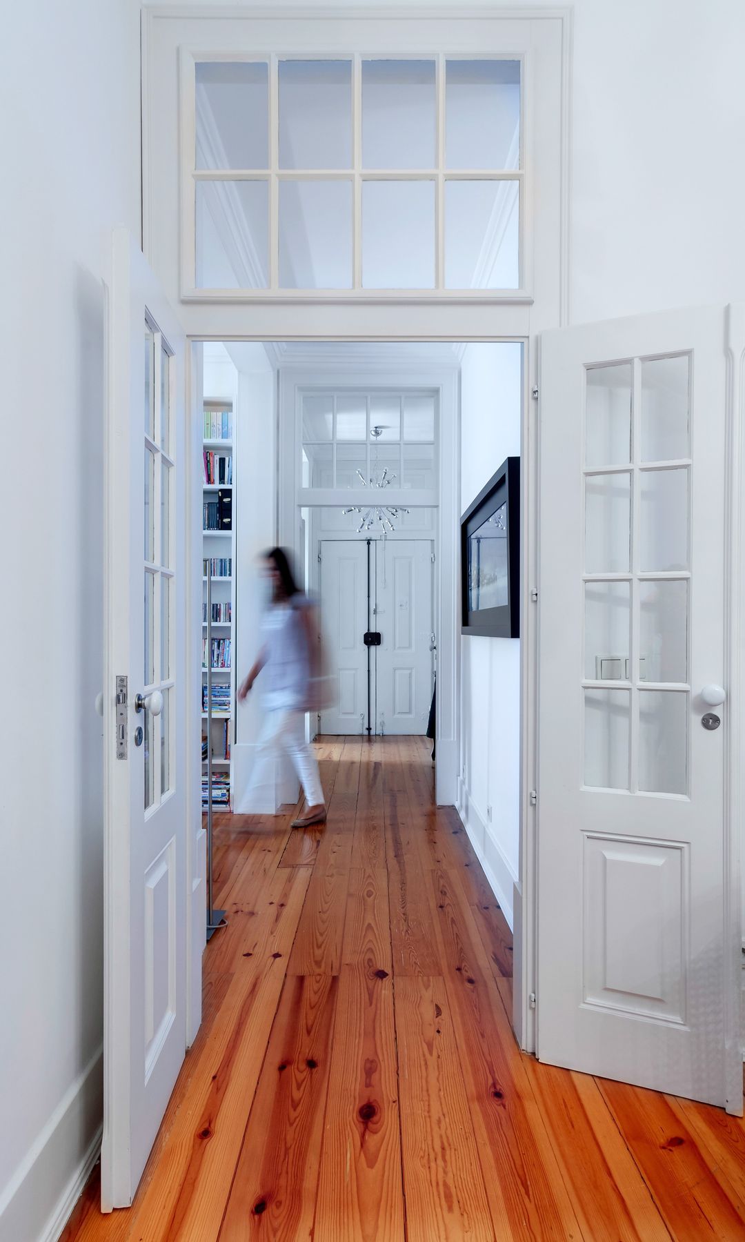 Pasillo con puertas blancas con cuarterones de cristal, suelo de madera, cuadro en la pared, mujer 