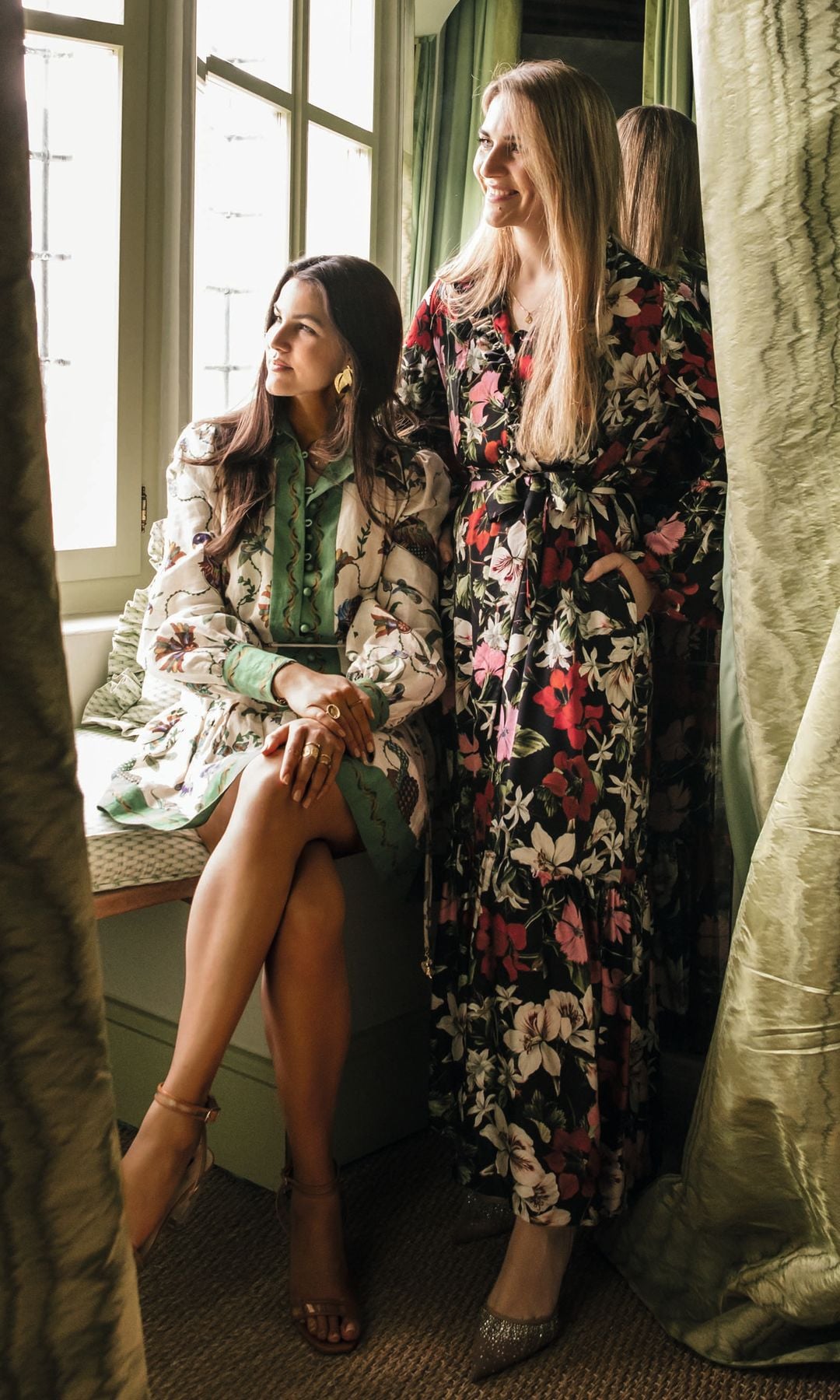 Vittoria y Philline en una ventana con cortinas verdes, una sentada y otra de pie.