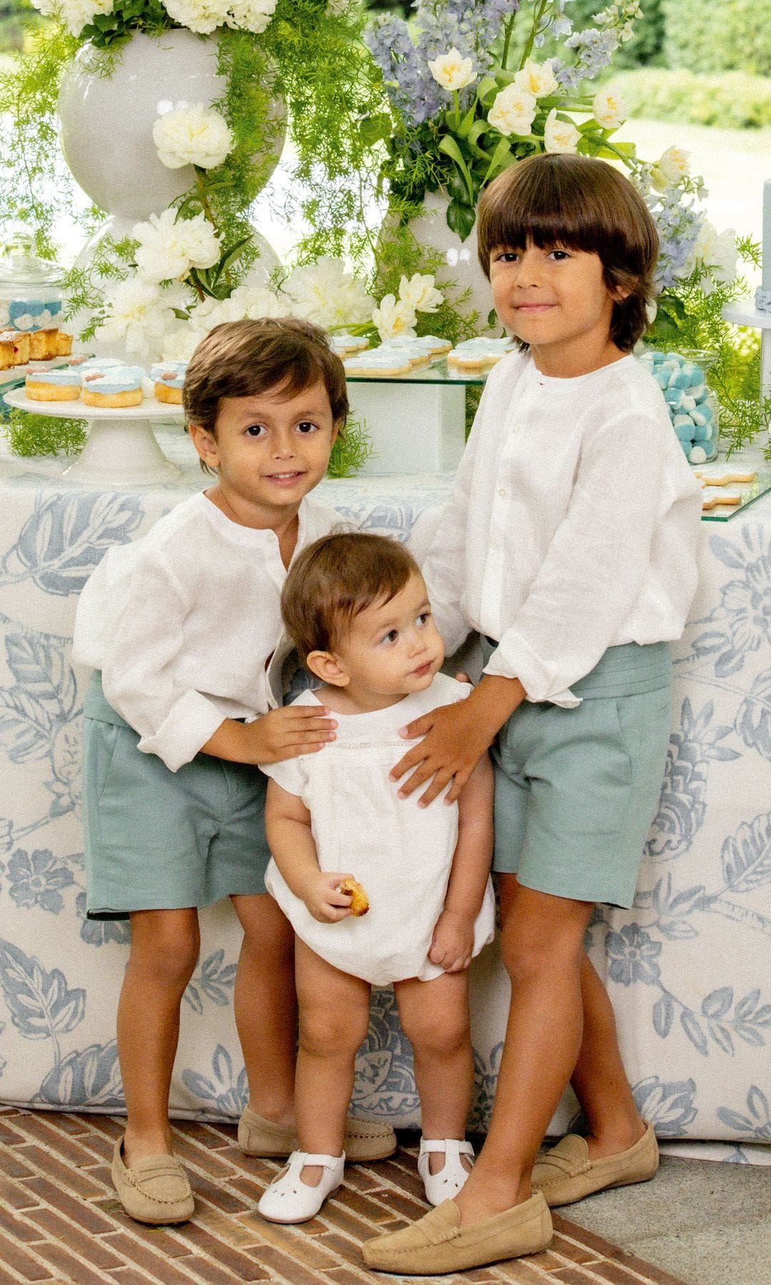 Miguel, de seis años, y Mateo, de cuatro y medio, miran divertidos a la cámara, frente a la mesa de postres, mientras cuidan con todo el cariño al benjamín de la familia. "Mis hijos están en edades muy divertidas y nos sorprenden cada día", nos confiesa Ana