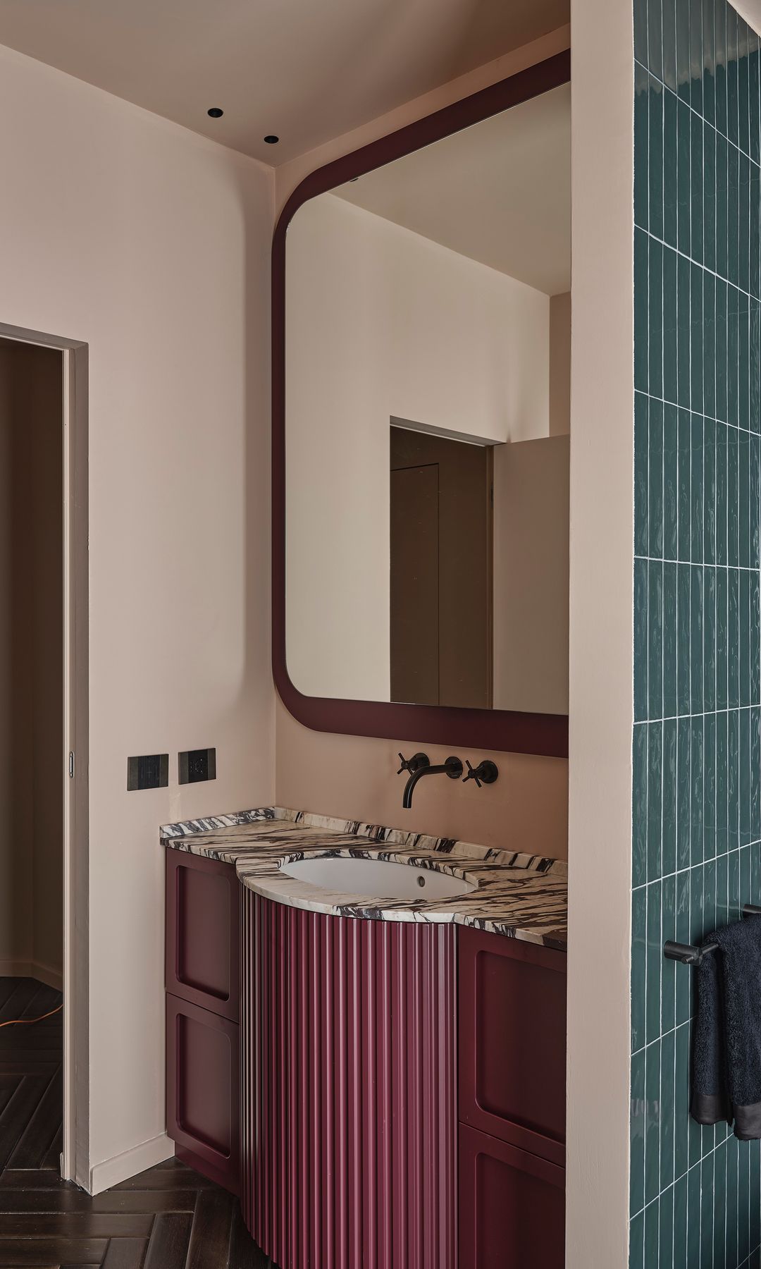 Baño con mueble bajolavabo burdeos, paredes de azulejos azules, suelo de madera, espejo con marco de madera