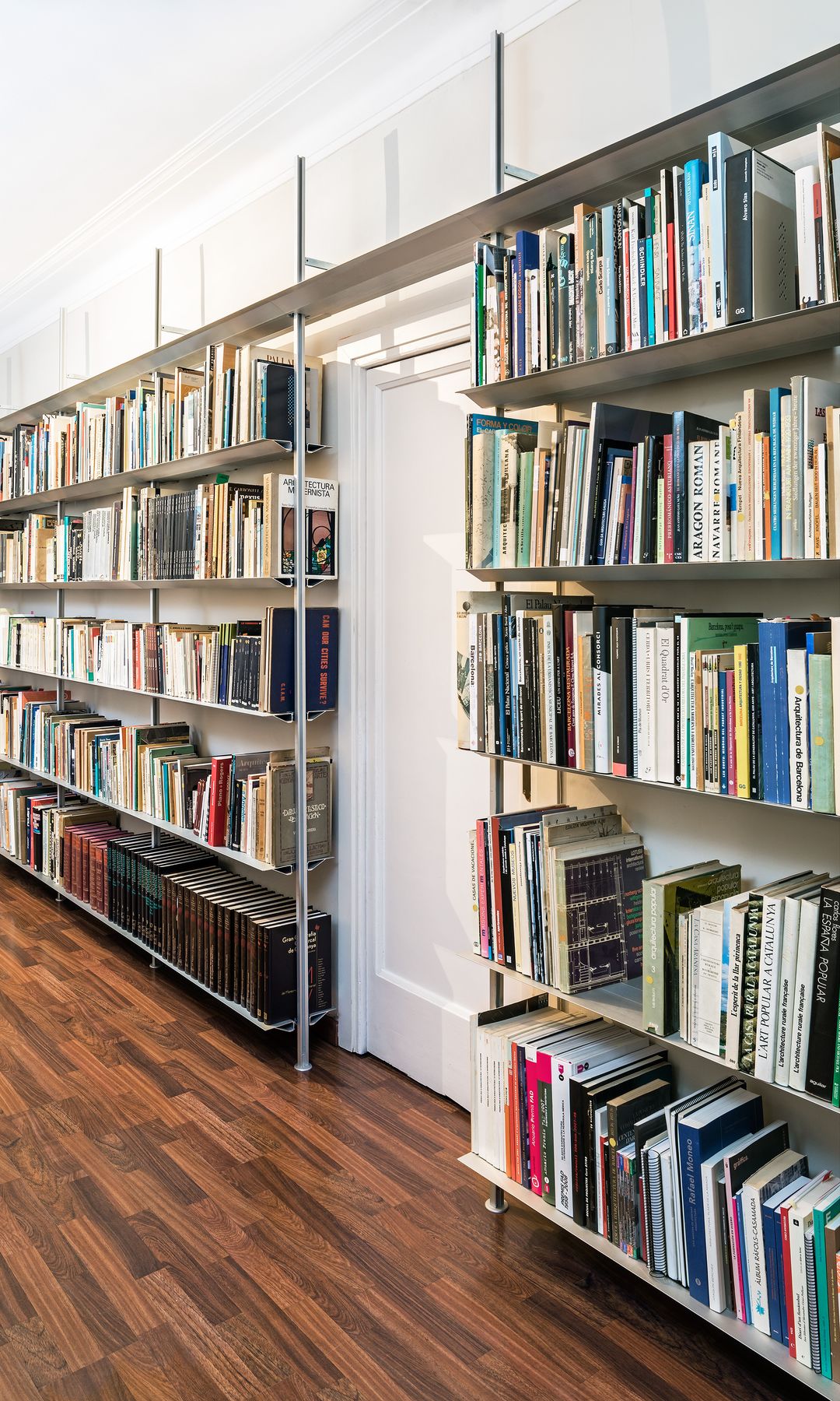 Librería de pared a pared sorteando la puerta de entrada, llena de libros, suelo de madera oscura 