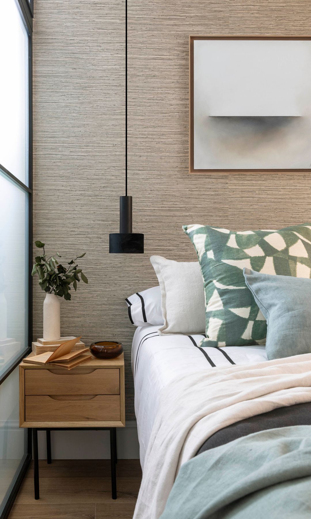 Dormitorio con revestimiento vinílico en la pared, lámpara de techo sobre la mesita de noche, mesita de noche de madera, jarrón 