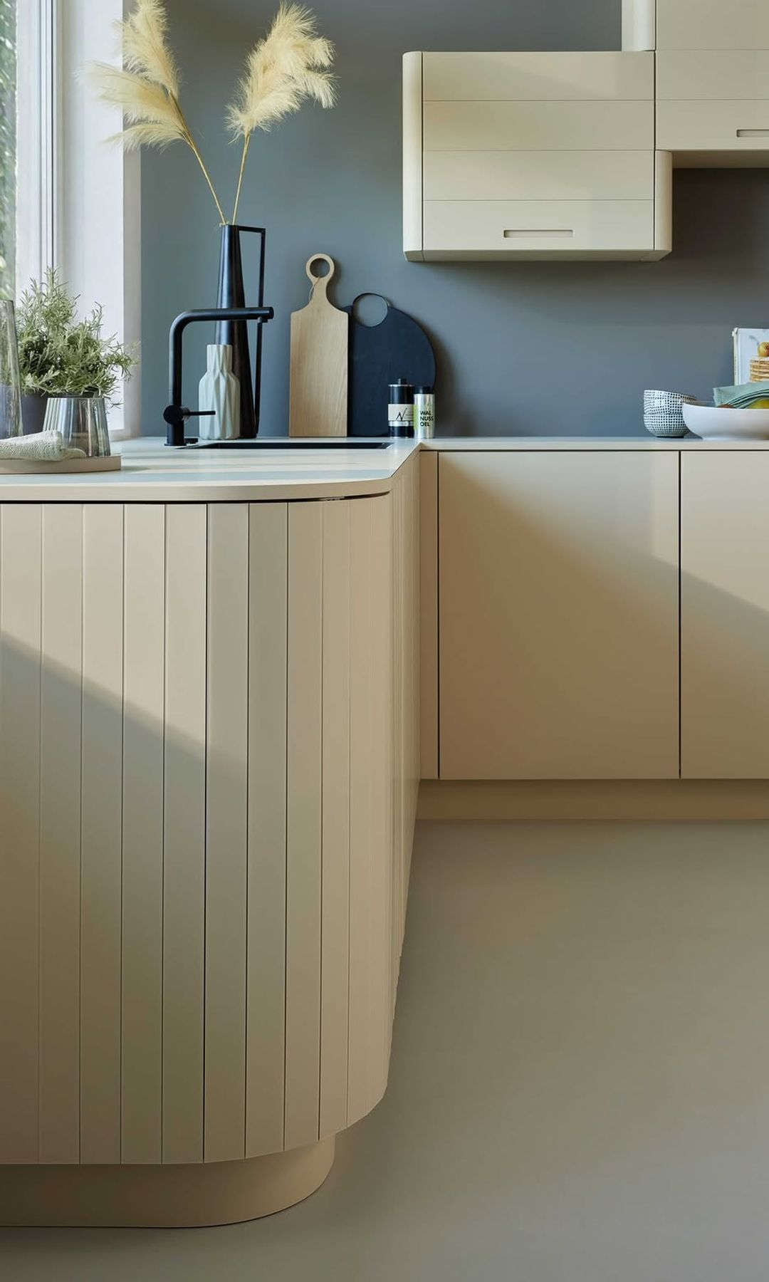 Cocina con mueble de formas curvas beige, pared en azul, tablas de cortar, florero