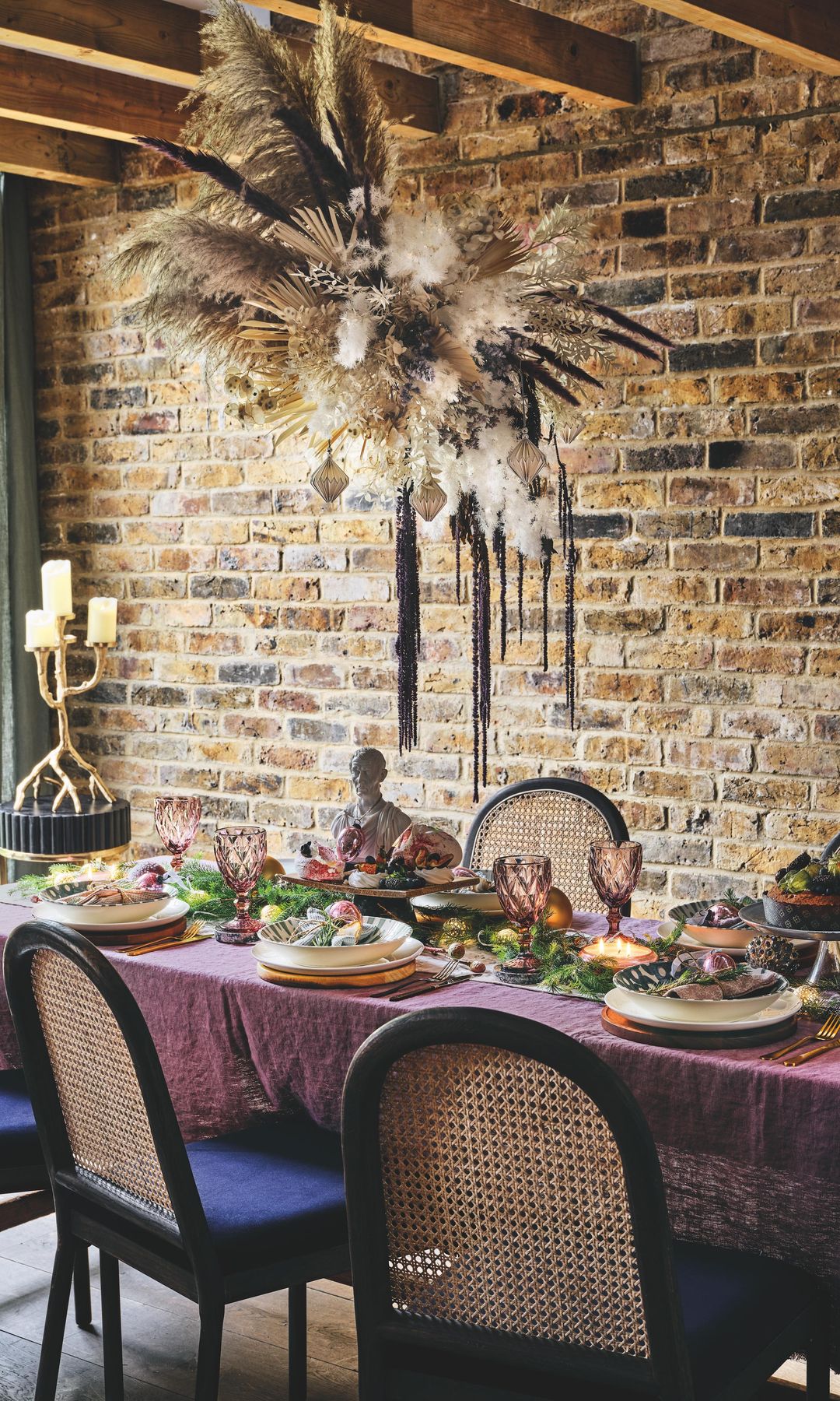 Mesa de Navidad con mantel burdeos, sillas de rejilla con asiento tapizado en azul, adorno de plumas colgando del techo, copas labradas en color burdeos