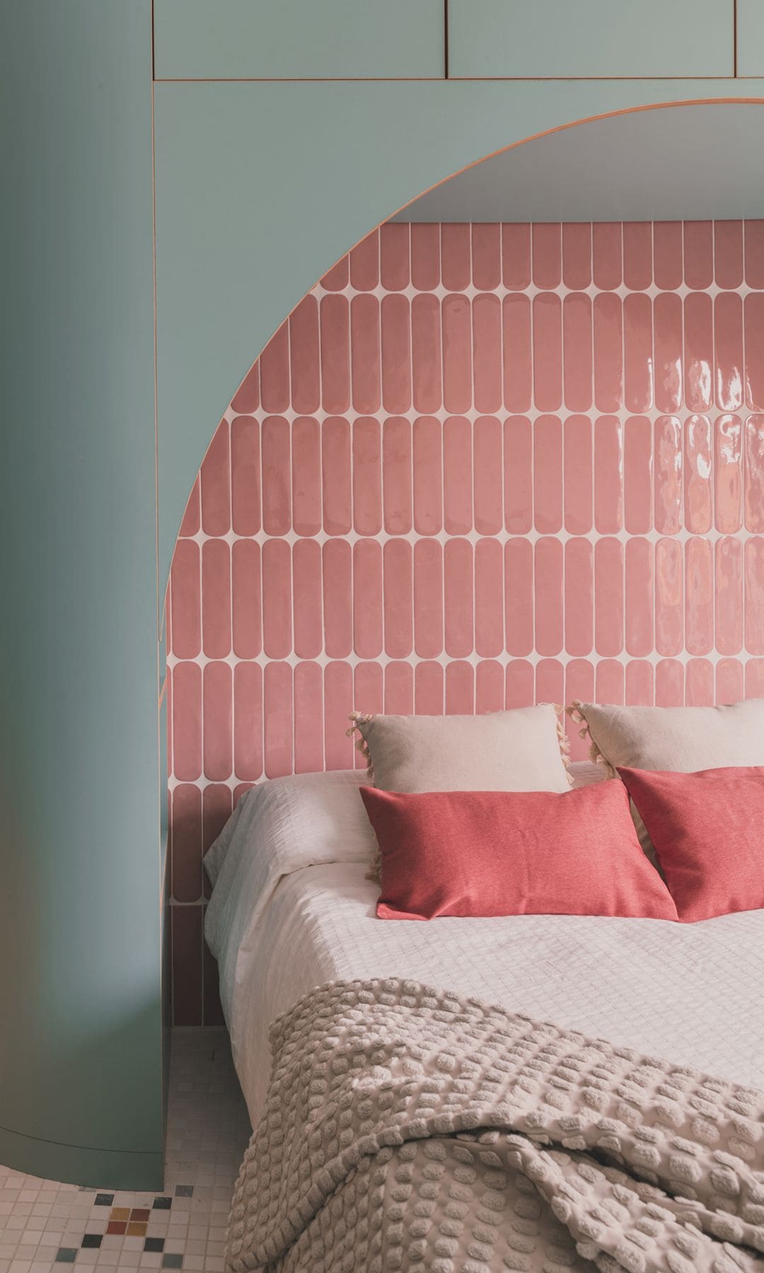 Cabecero a medida con estructura de madera azul de forma redondeada y pared de azulejos rosas brillantes, cojines
