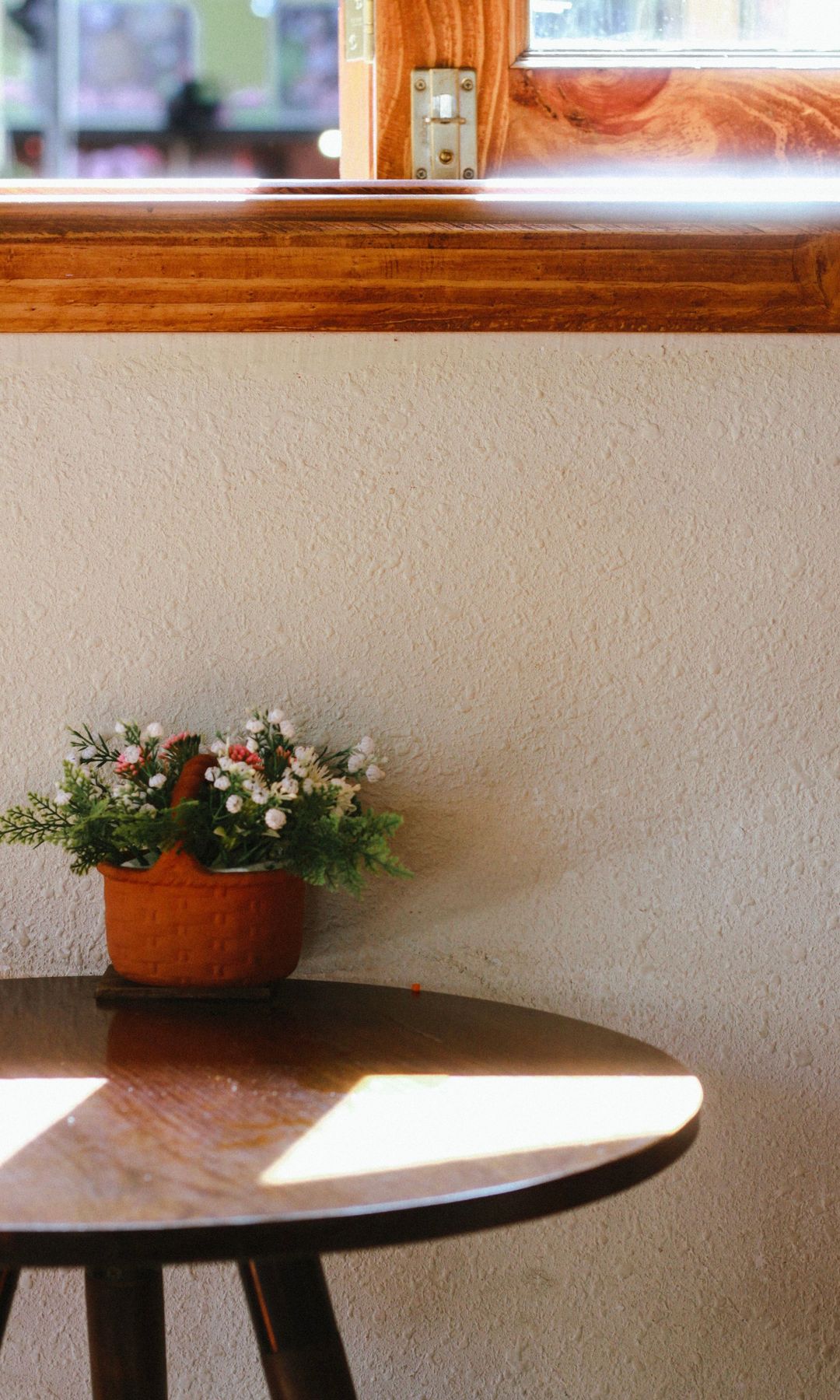 Pared con gotelé, mesa redonda de madera con maceta, ventana con perfiles de madera