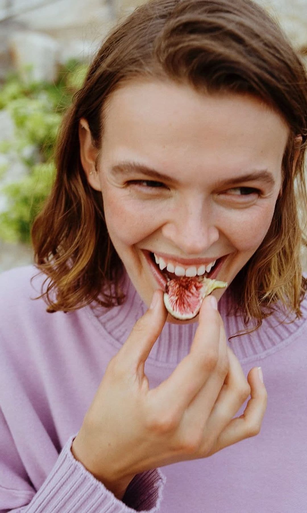 Mujer riendo mientras come un higo fresco.