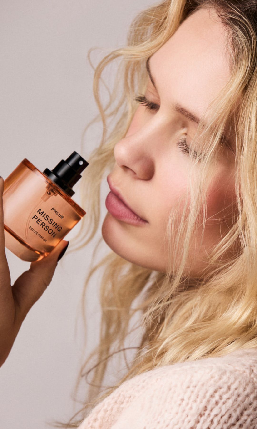 Mujer sosteniendo el perfume Missing Person de Phlur cerca del rostro
