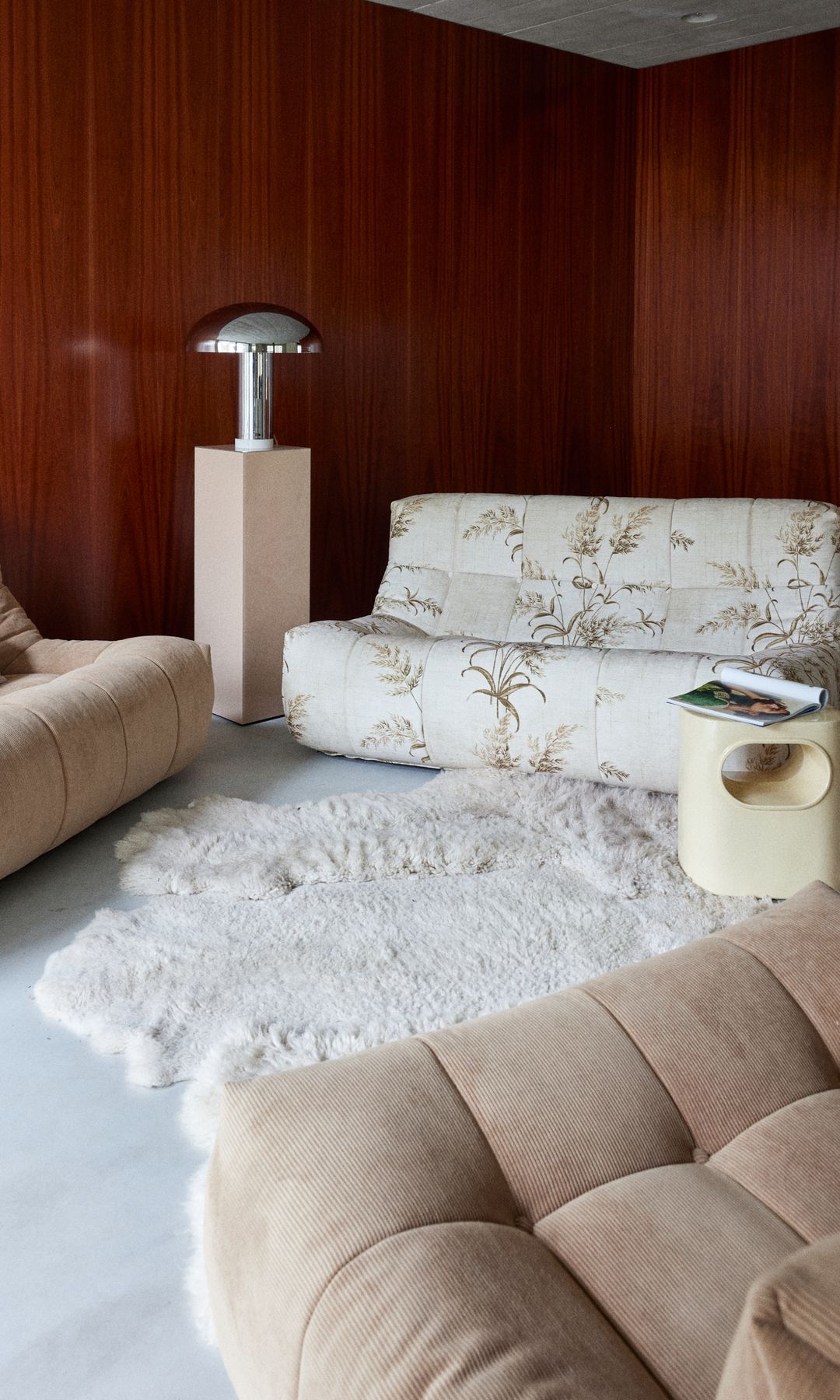 Salón con alfombra de pelo blanco, lámpara de sobremesa metalizada, sofá blanco con estampado