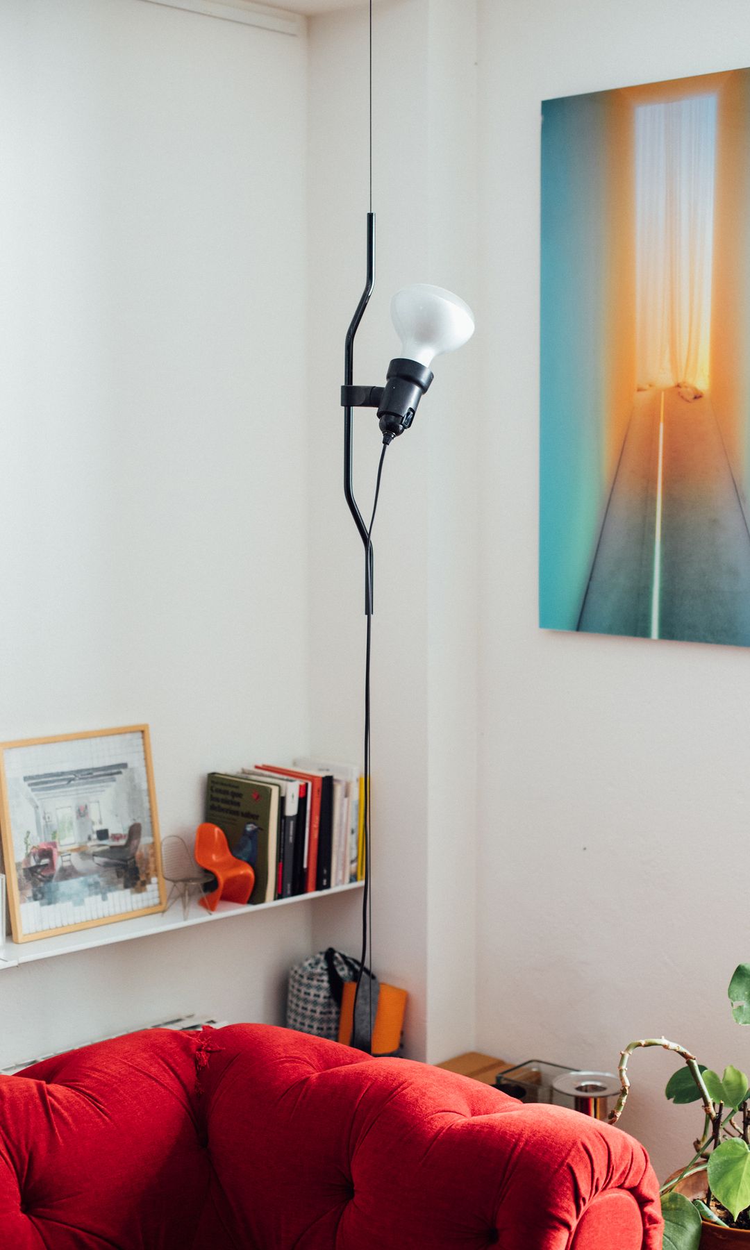 Salón con cuadro en la pared, sofá rojo, balda con cuadros y libros, lámpara de techo en forma de bombilla