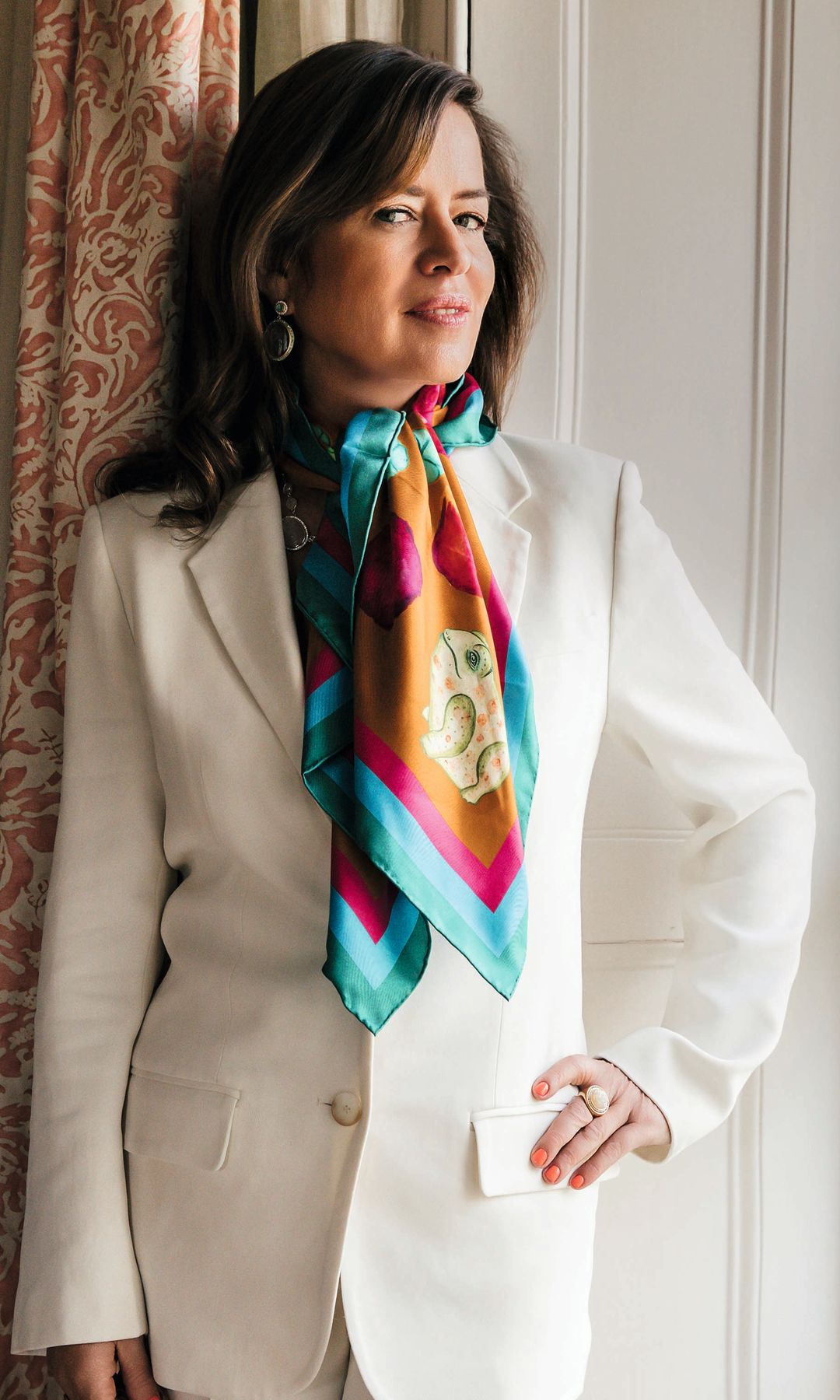 Jade Jagger posa junto a una ventana con traje blanco y pañuelo colorido