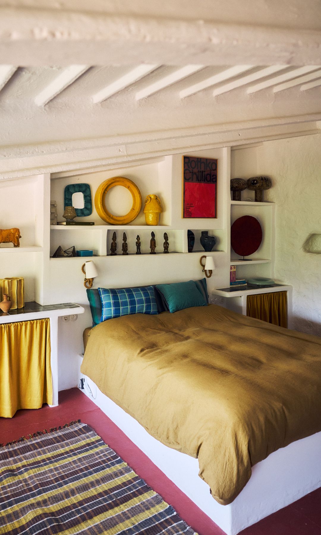Dormitorio con cabecero de obra con baldas, ropa de cama amarillo mostaza, cortinillas en lugar de puertas