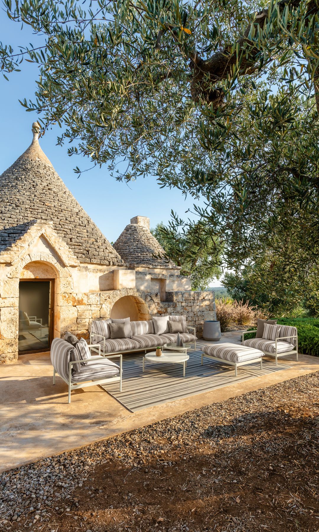 Casa con jardín y salón exterior con alfombra, muebles de aluminio y asientos de rayas