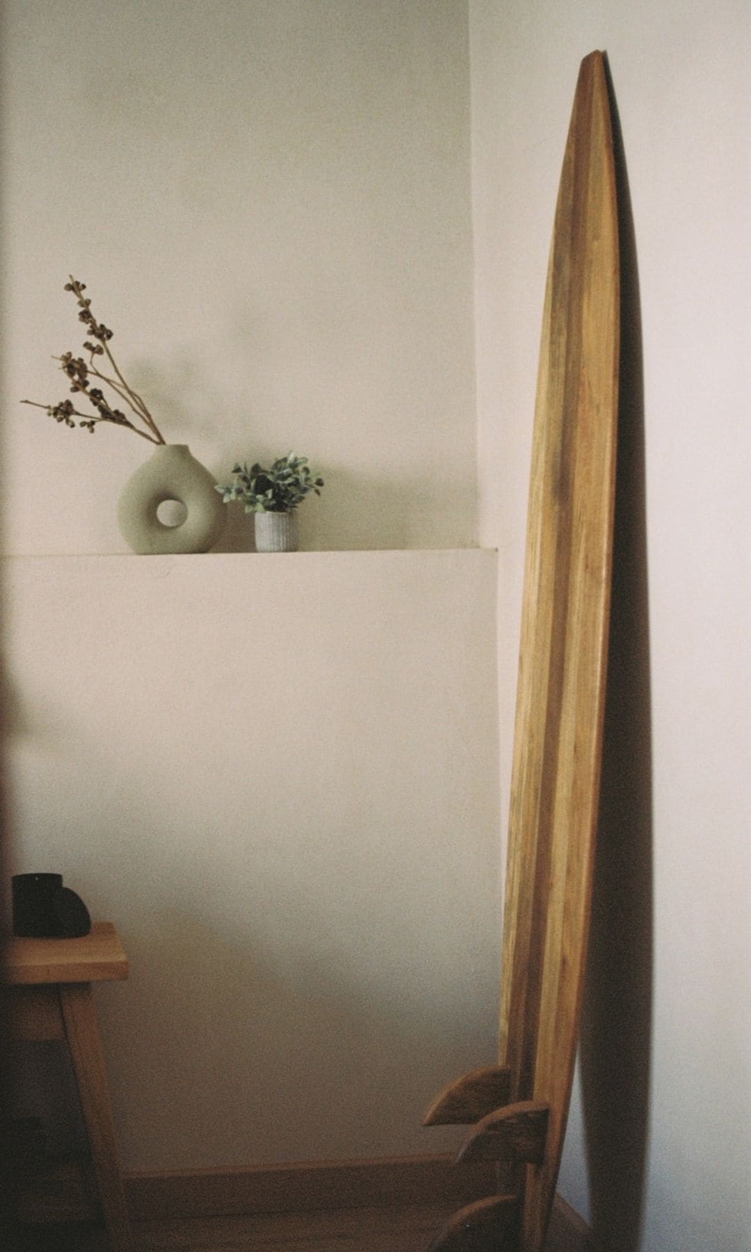 Dormitorio con cabecero de obra de pared a pared, jarrón con flores, mesita de noche de madera, tabla de surf apoyada en la pared