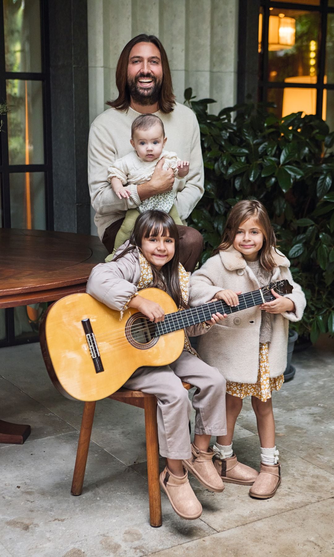 Juan Carmona con cabello largo sostiene a su bebé, mientras sus otras dos niñas tocan la guitarra sentadas junto a él