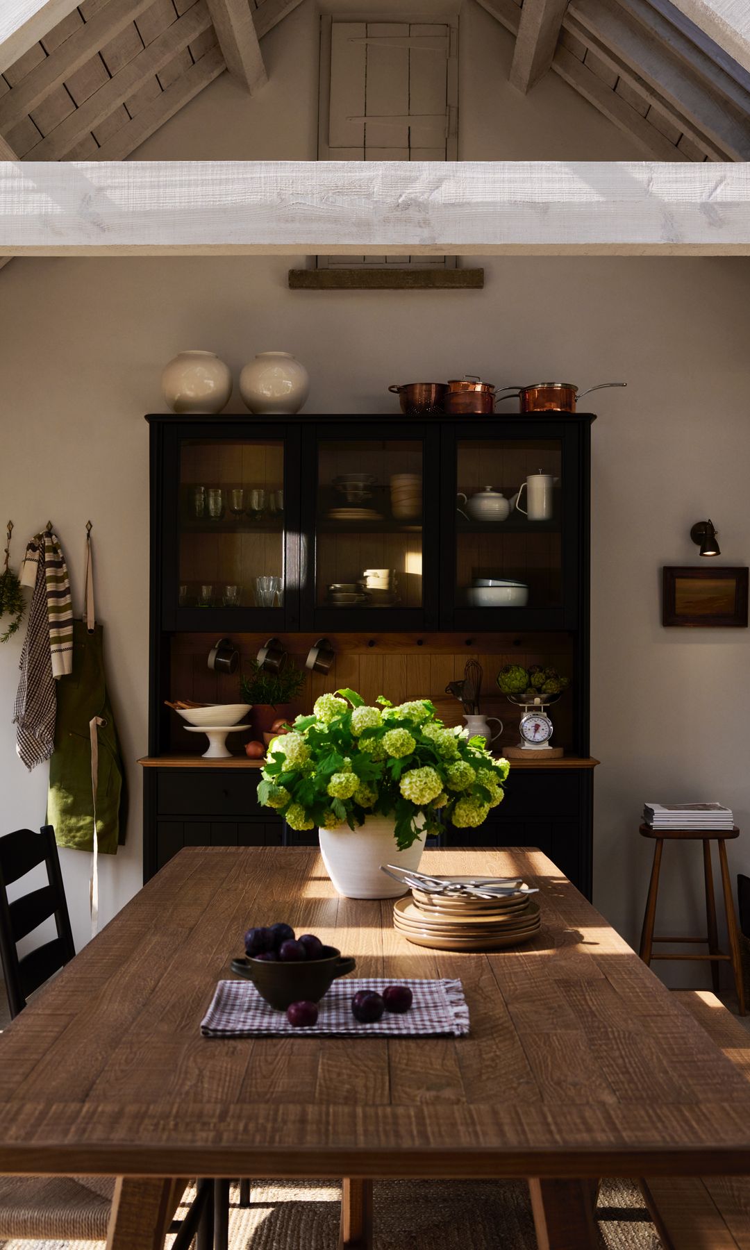Cocina con alacena y mesa de madera con jarrón con flores, trapo de cocina de cuadros