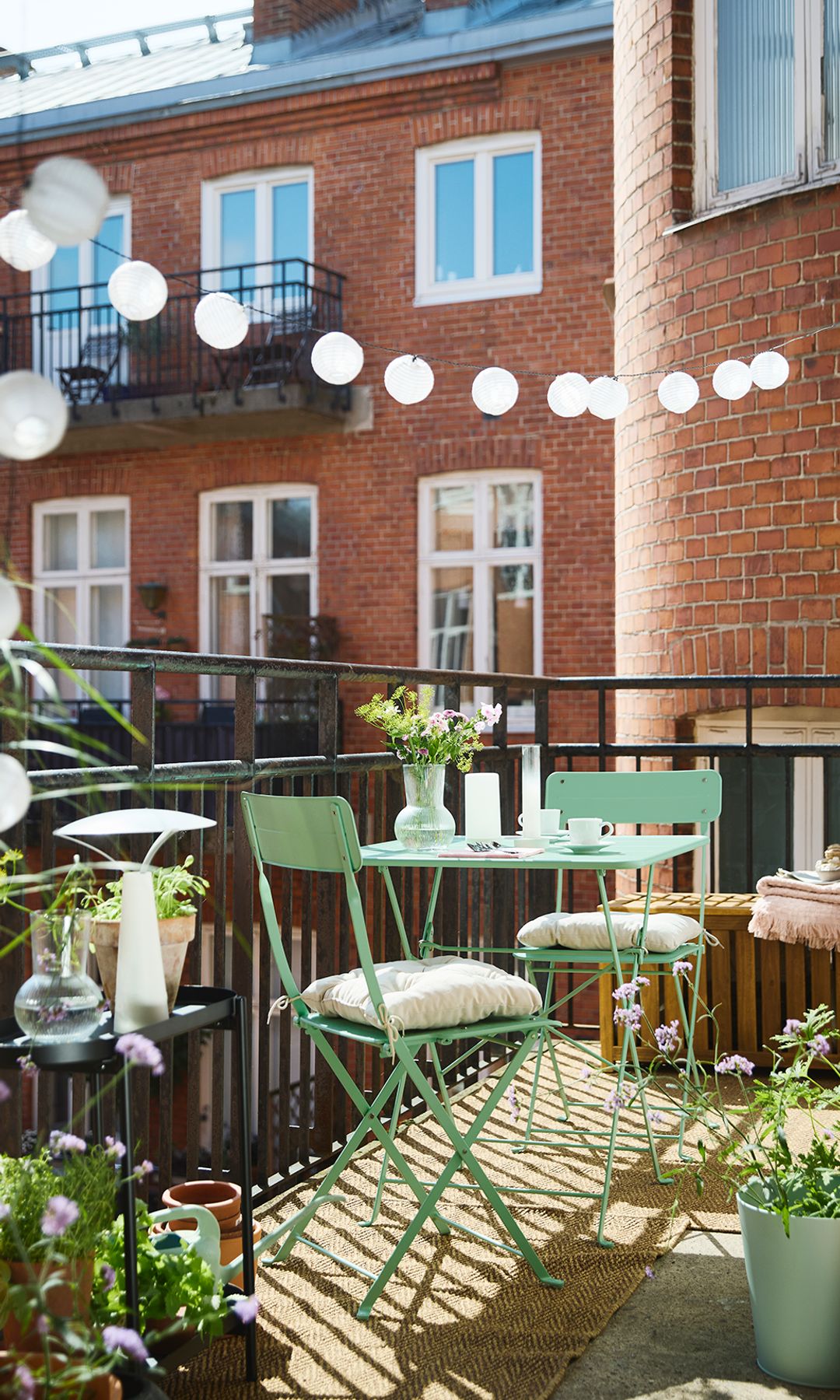 Balcón con muebles de hierro verde de IKEA plegables y guirnalda de luces