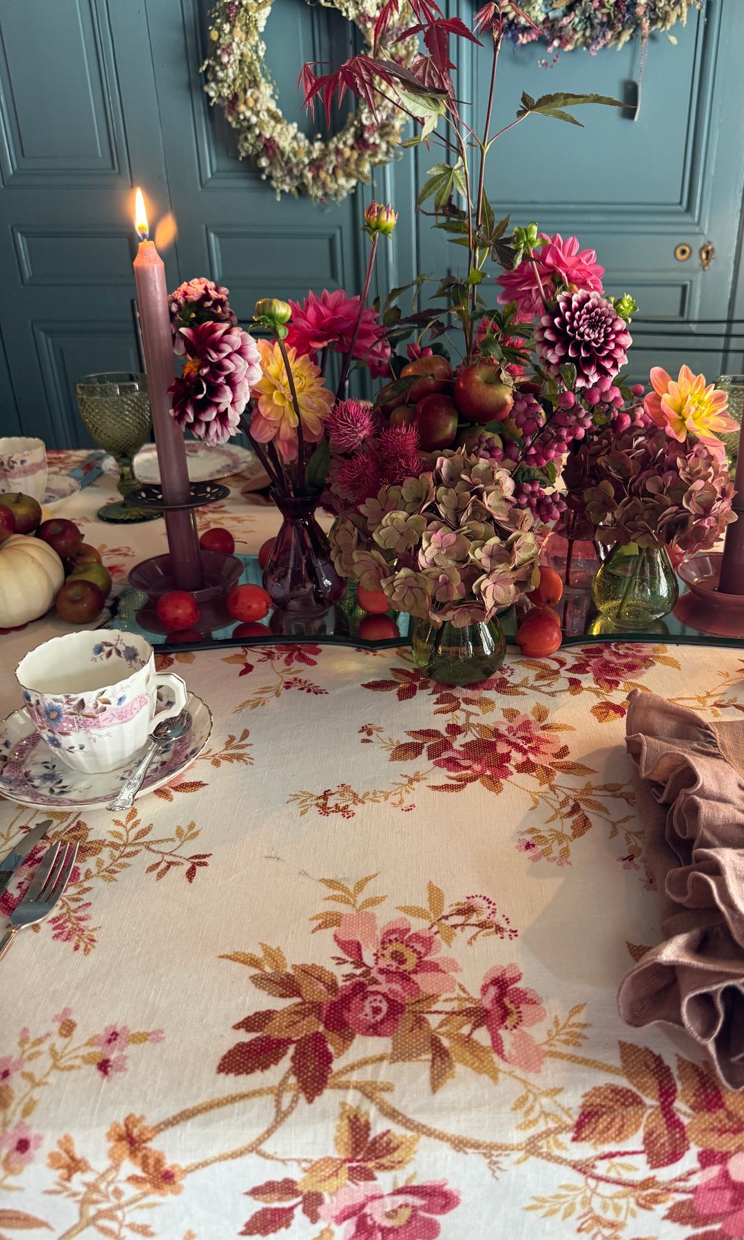Mesa de comedor con mantel de flores, taza de café, candelabros morados, centro de mesa con hortensias, dalias y otras flores
