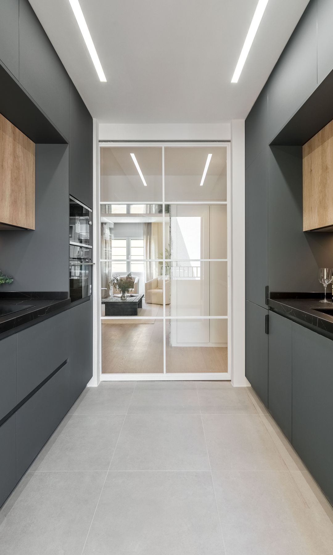 Cocina en paralelo con muebles negros, puerta corredera de cristal con marco blanco, luces led en el techo