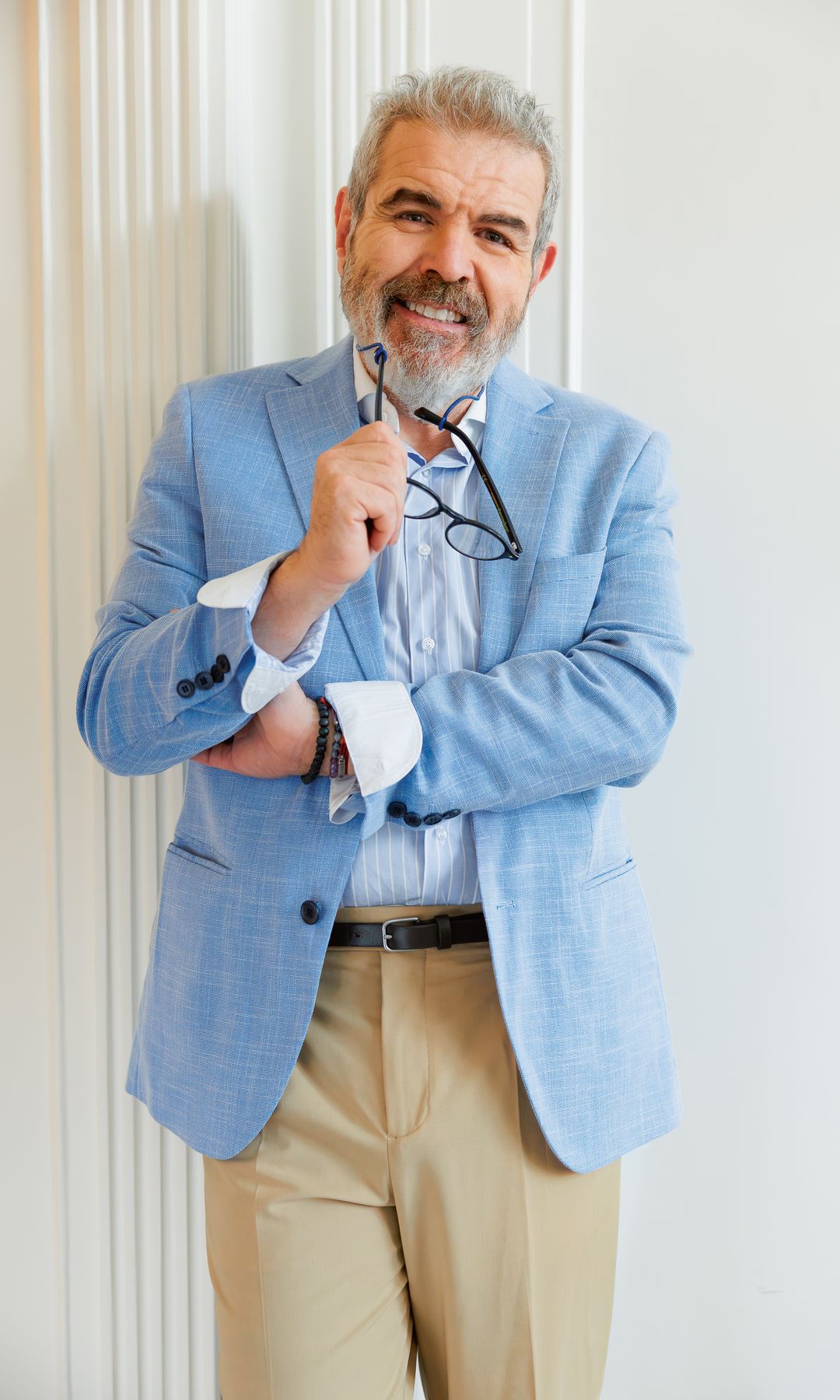 Lorenzo Caprile con barba y cabello gris, vistiendo traje azul, sosteniendo gafas.
