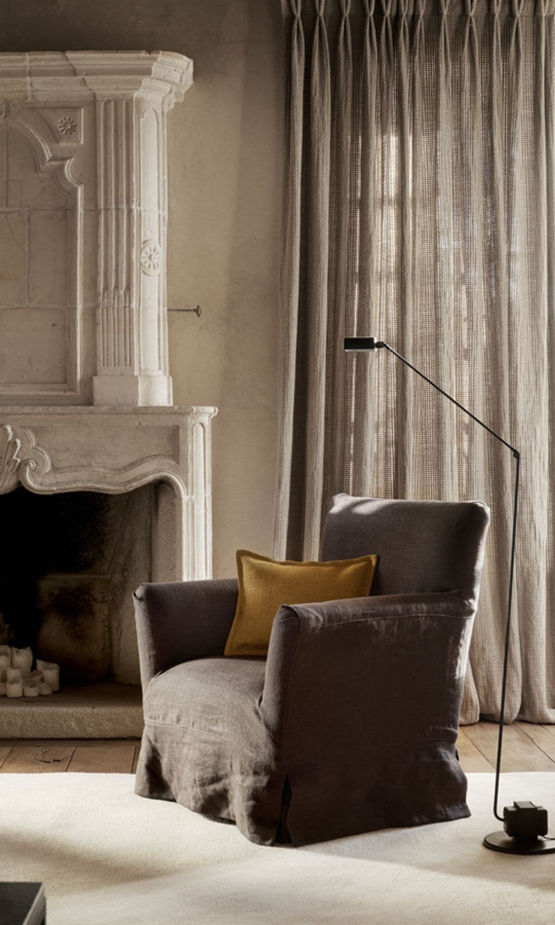 Salón con chimenea, butaca marrón, cortinas beiges, alfombra, lámpara de pie