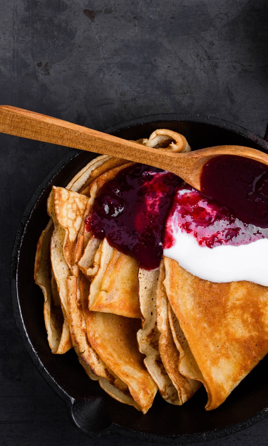 Sartén de hierro fundido con crêpes con nata y mermelada de fresa en su interior