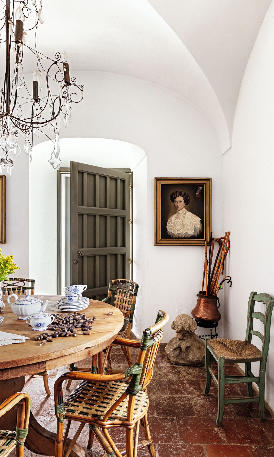 Comedor con mesa redonda, sillas de mimbre, cuadros de personas en la pared y puerta verde.