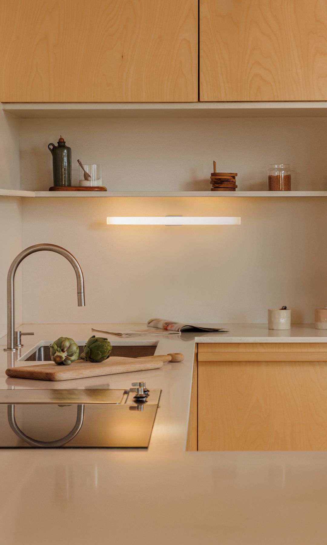 Cocina de madera, encimera blanca, con aplique de pared bajo los armarios superiores, balda 