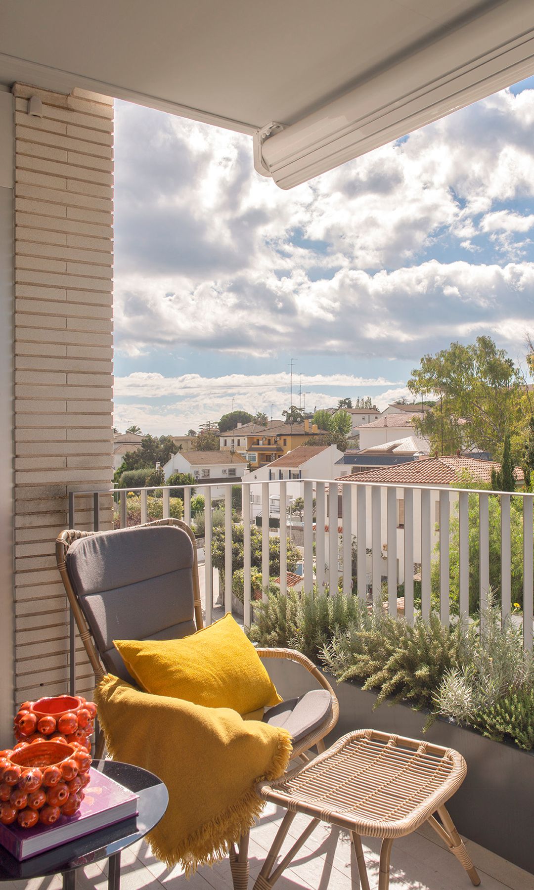 Terraza con butaca de fibras vegetales con reposapiés, cojín amarillo, manta amarilla, adornos rojos, maceteros con plantas 