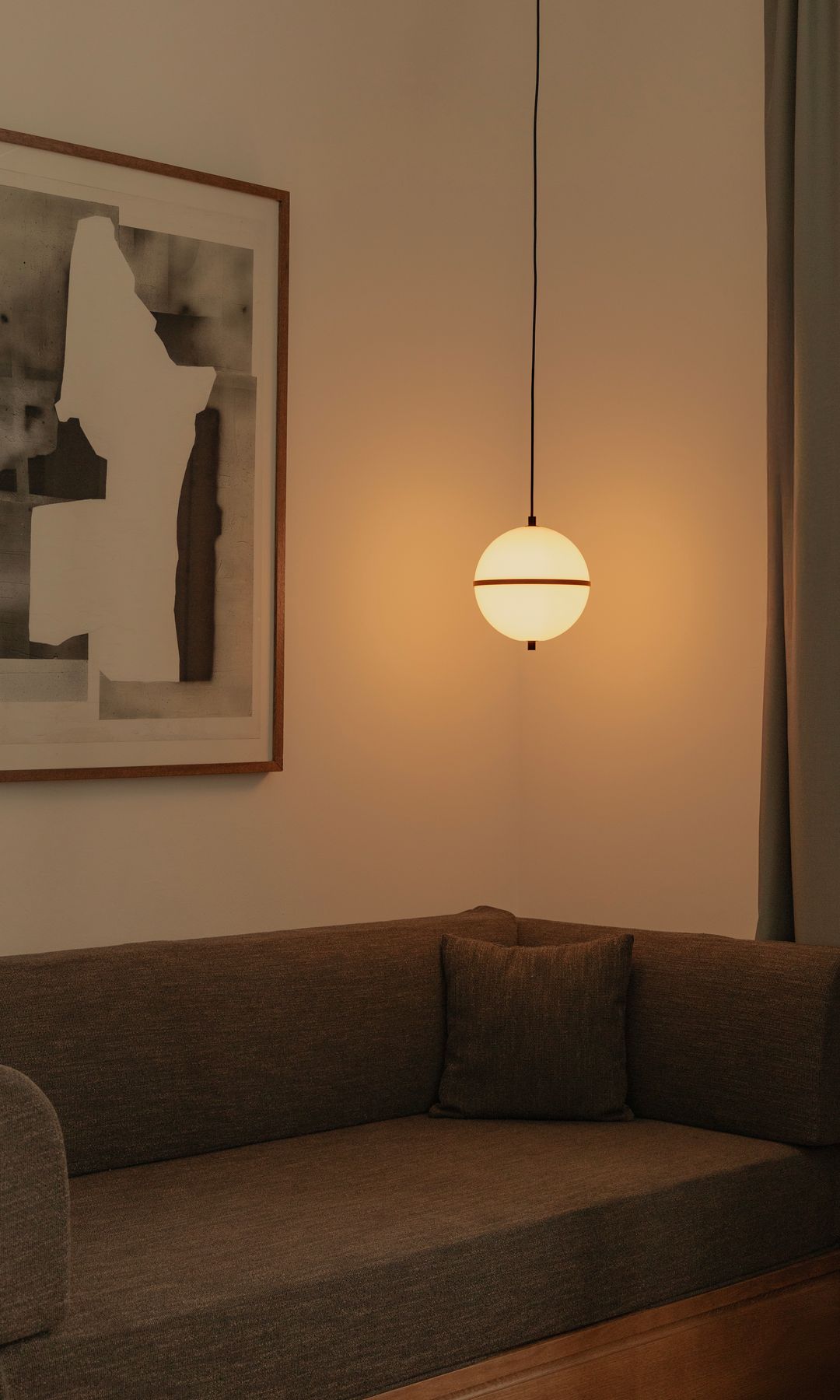 Sofá marrón con lámpara de techo encendida en uno de sus lados, cuadro en la pared del sofá y cortinas