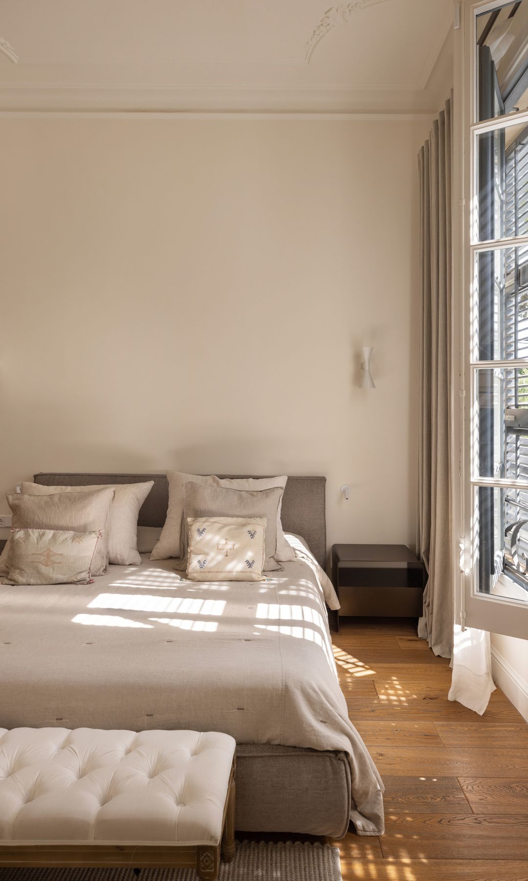 Dormitorio principal con ventana abierta, banqueta a los pies de la cama, suelo de madera, visillos