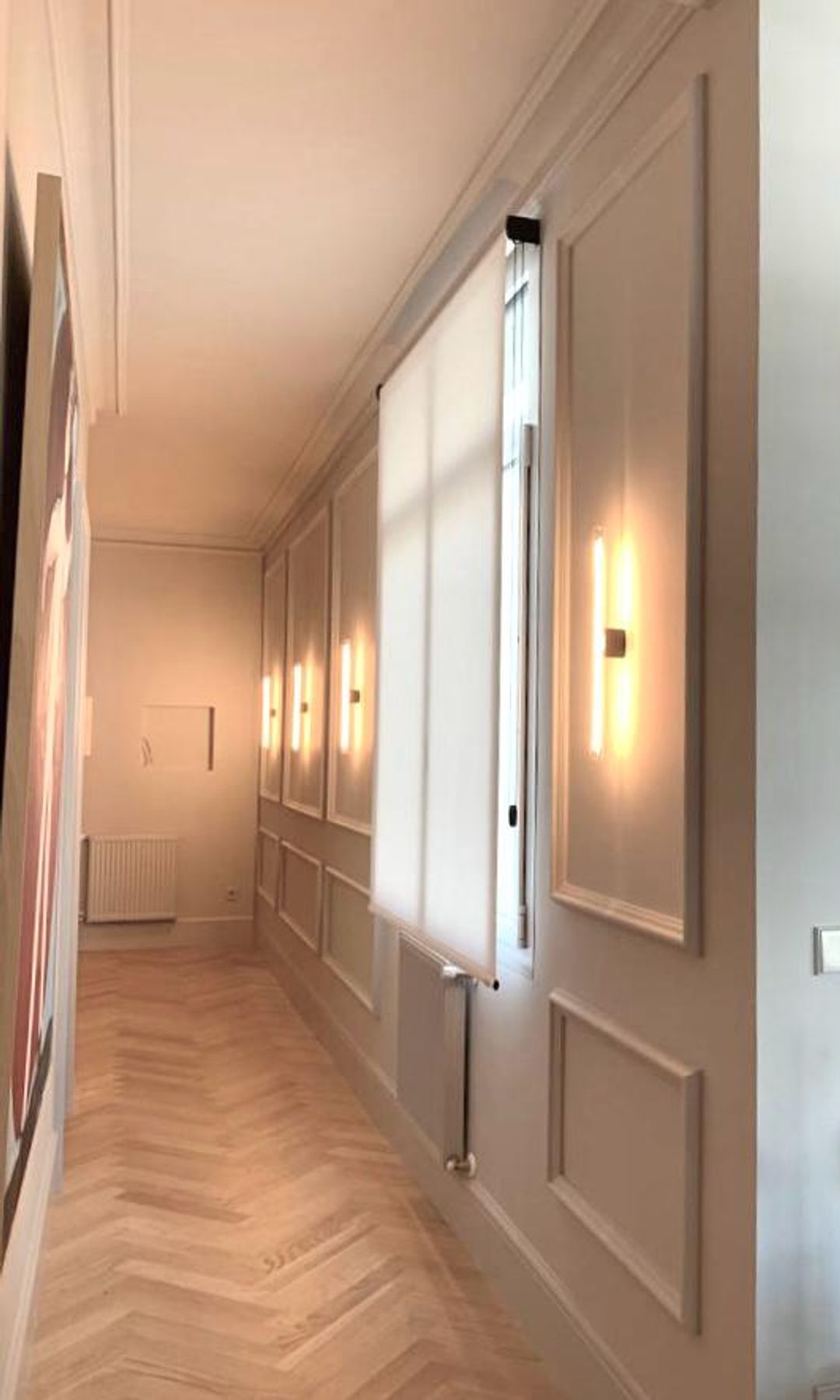Pasillo con molduras y apliques en las paredes, suelo de madera en espiga, ventana con estor, molduras en el techo 